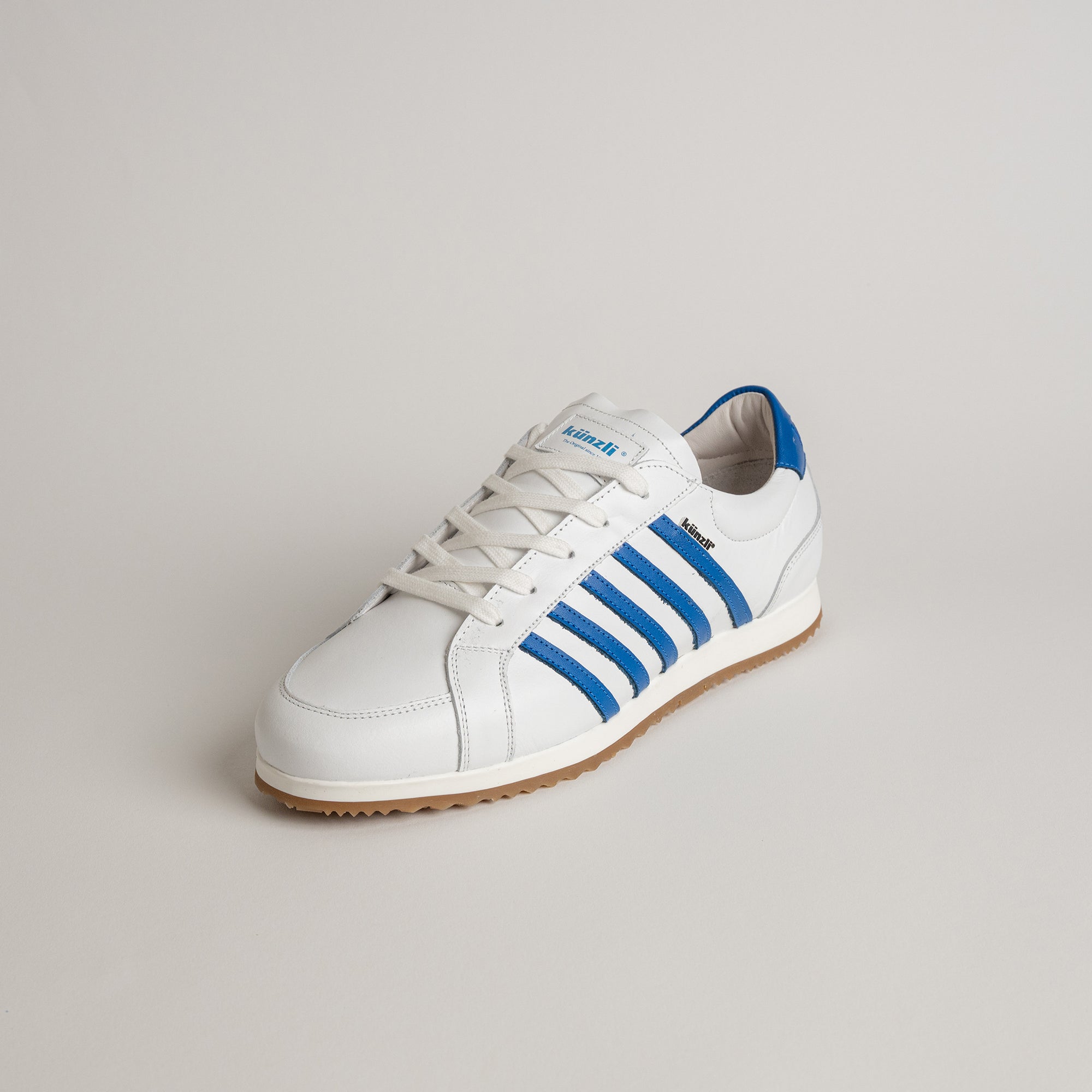 Weißer Kuenzli Schuh mit blauen Streifen auf hellem Hintergrund.