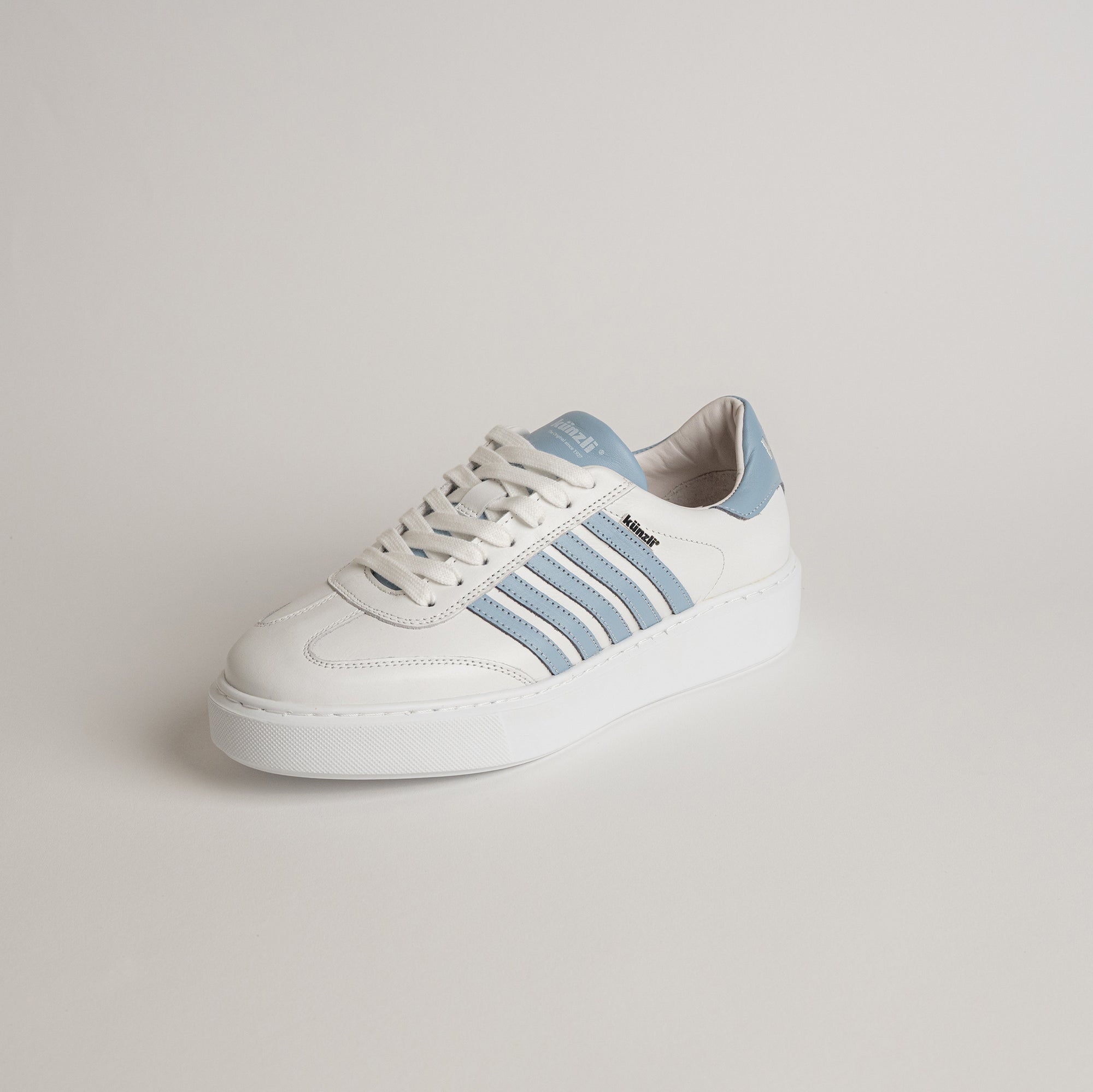 Weißer Sneaker mit blauen Streifen von Kuenzli Schuhe auf hellem Hintergrund.