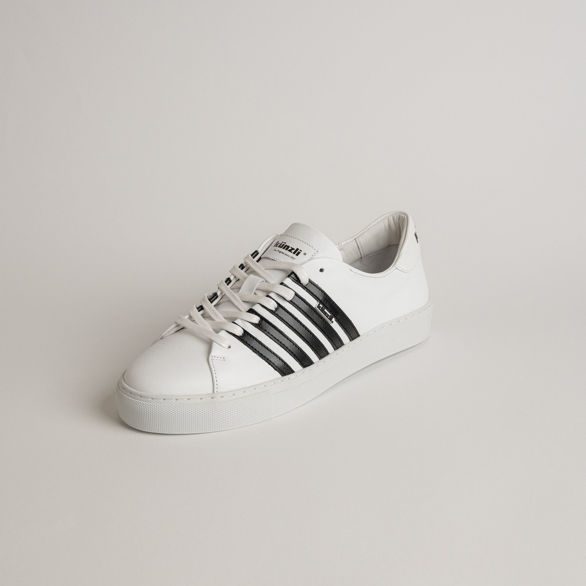 Weißer Kuenzli Schuh mit schwarzen Streifen auf hellem Hintergrund.