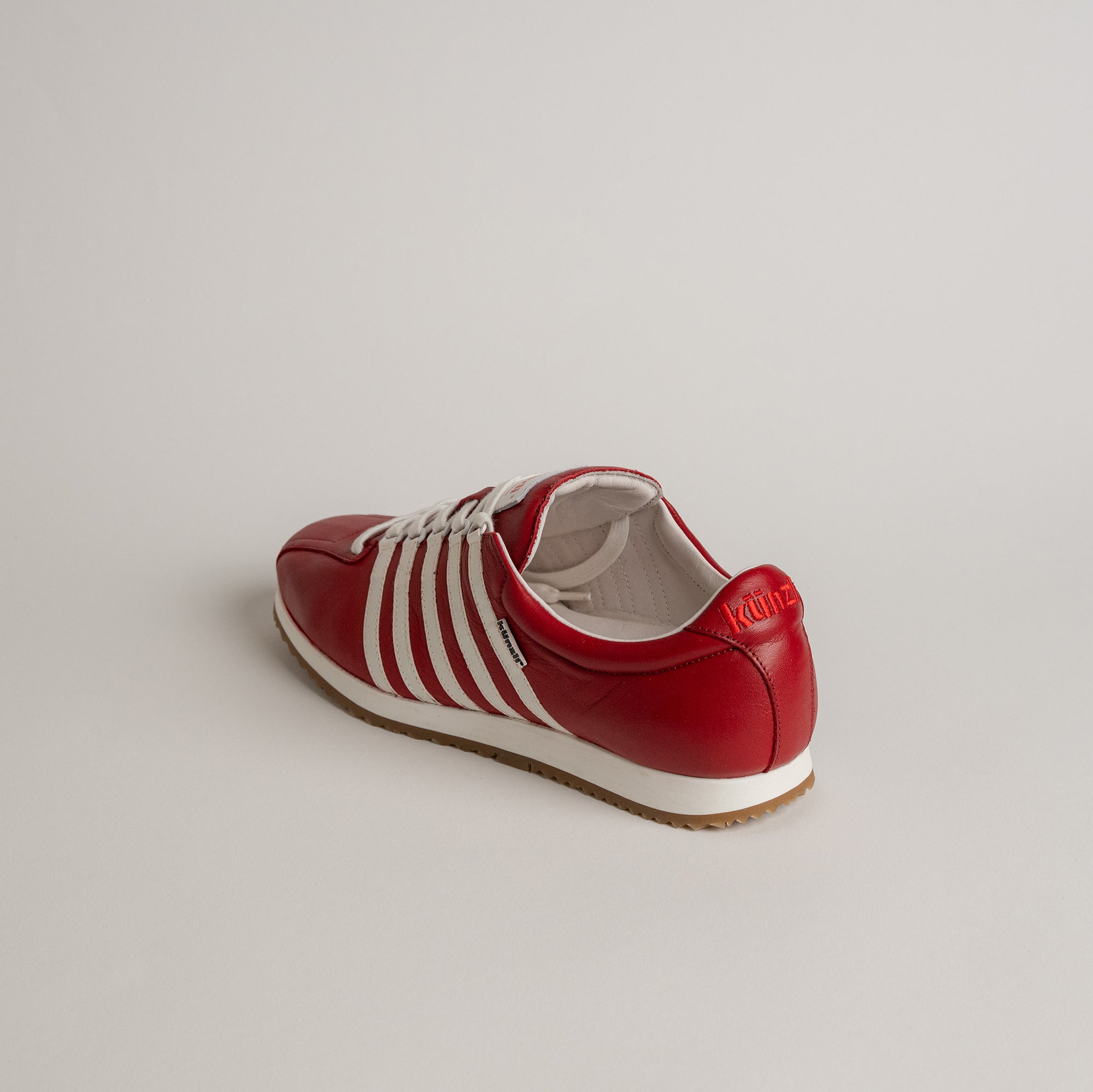 Roter Kuenzli Schuh aus Leder mit weißen Streifen auf hellem Hintergrund.