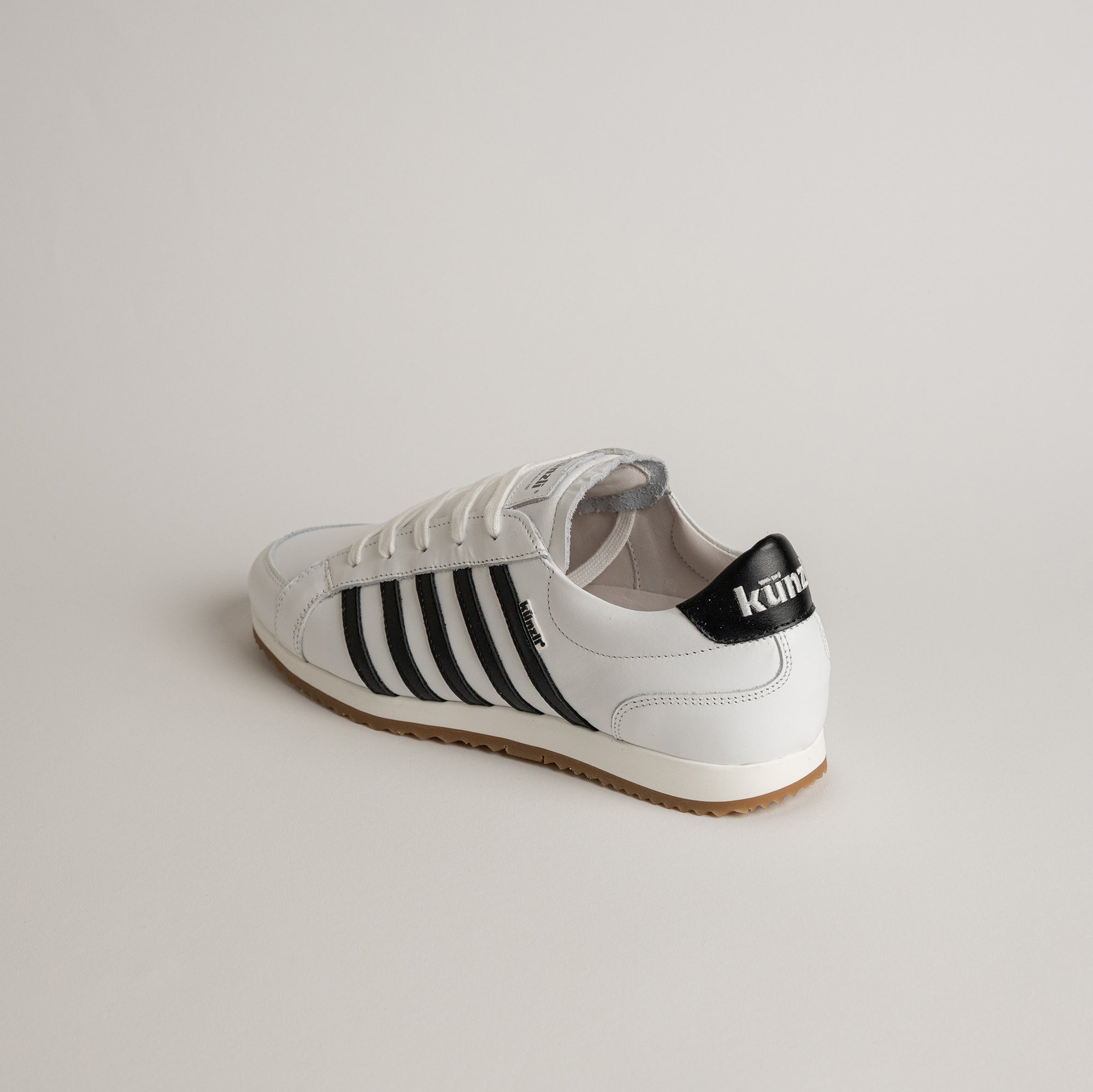 Weißer Kuenzli Schuh mit schwarzen Streifen auf hellem Hintergrund.