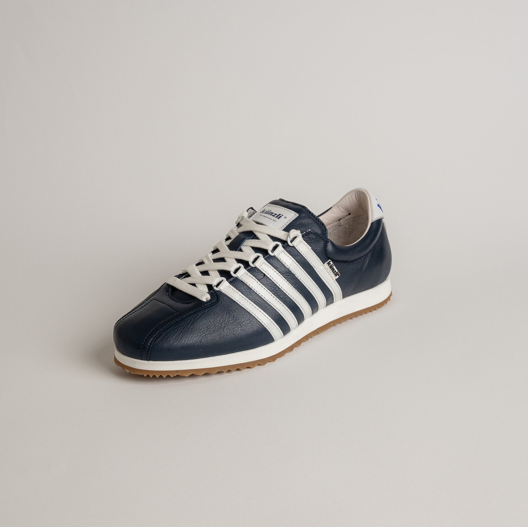 Ein dunkelblauer Lederschuh von Kuenzli Schuhe mit weißen Streifen auf hellem Hintergrund.