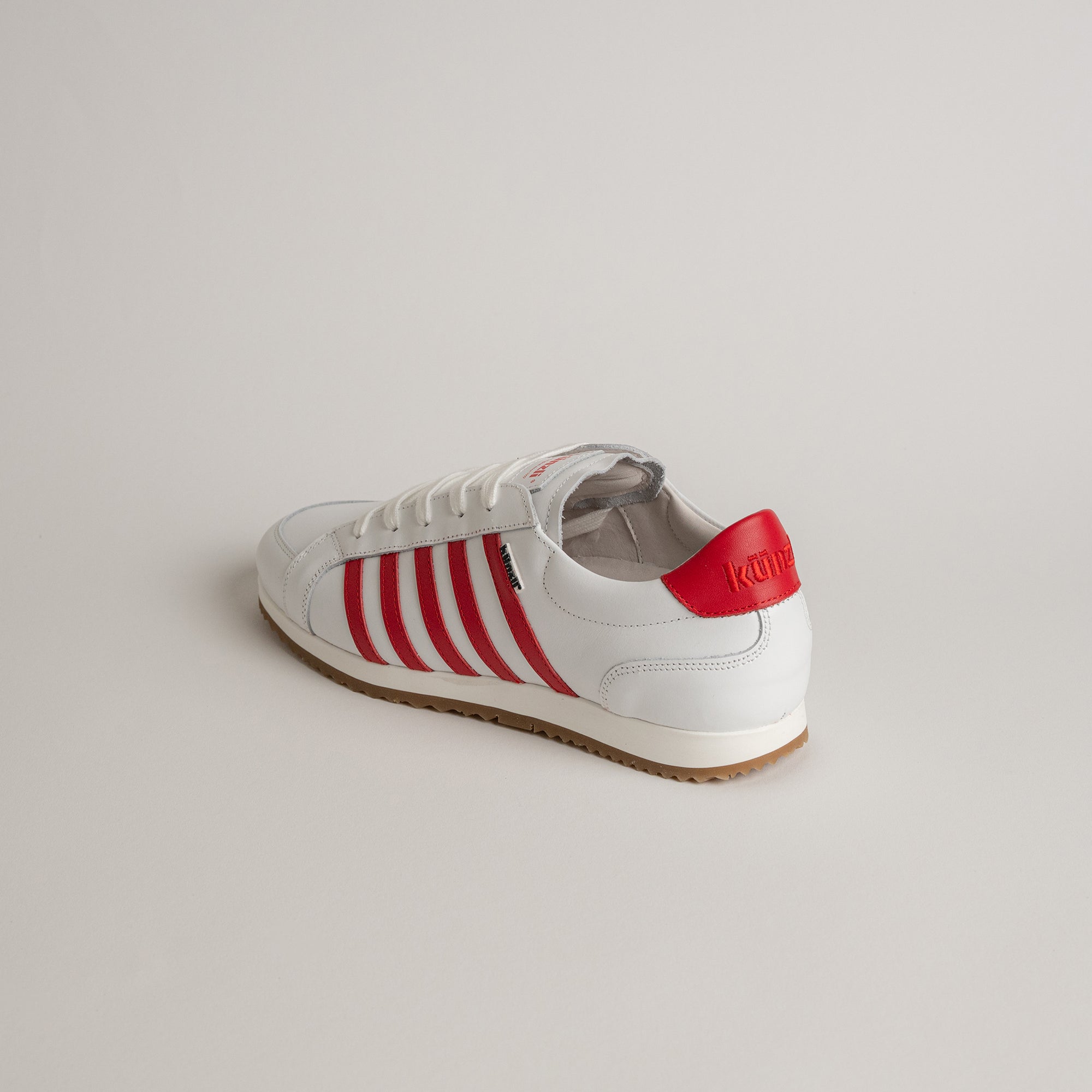 Weißer Kuenzli Schuh mit roten Streifen und Logo auf hellem Hintergrund.