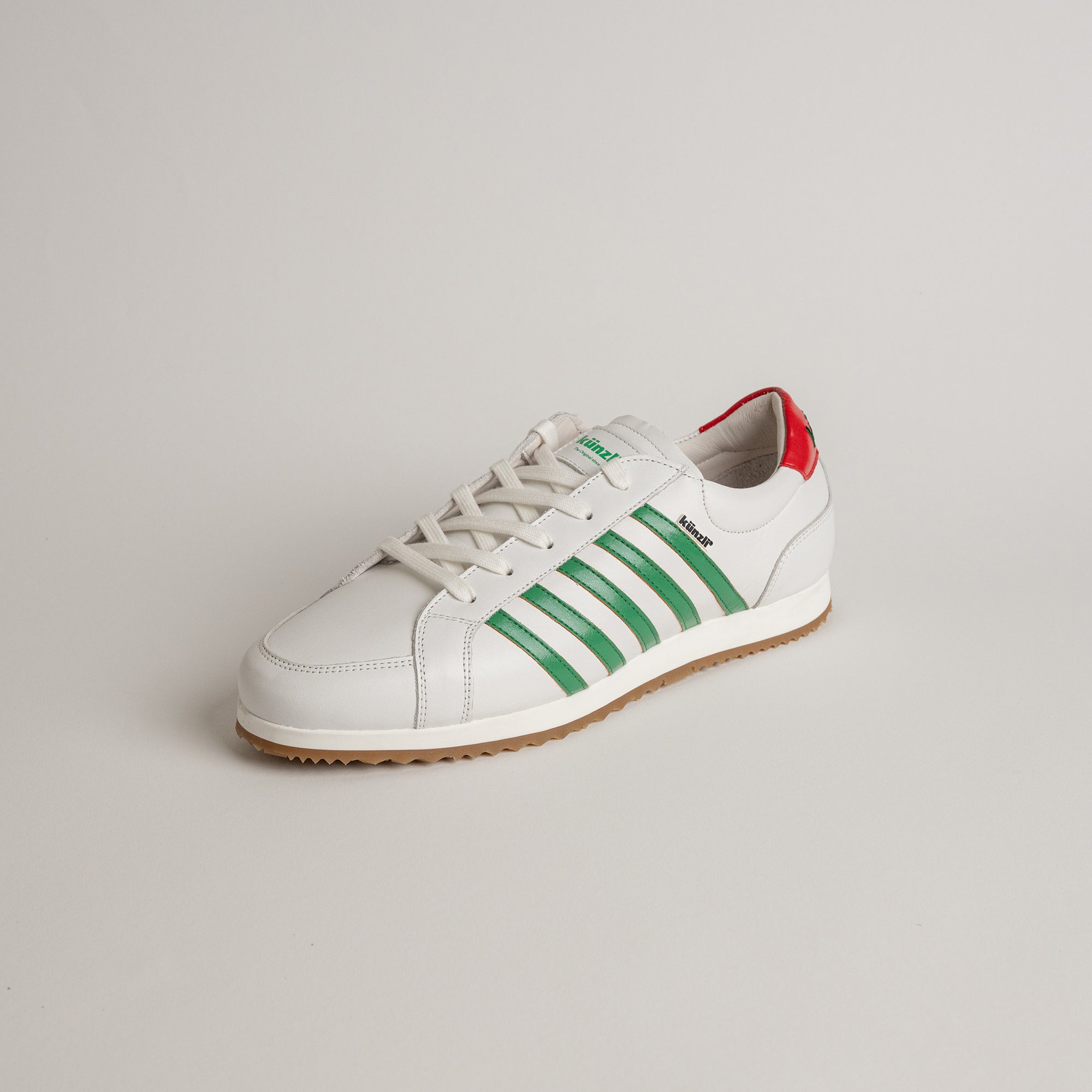 Weißer Kuenzli Schuh mit grünen Streifen und rotem Detail auf hellem Hintergrund.