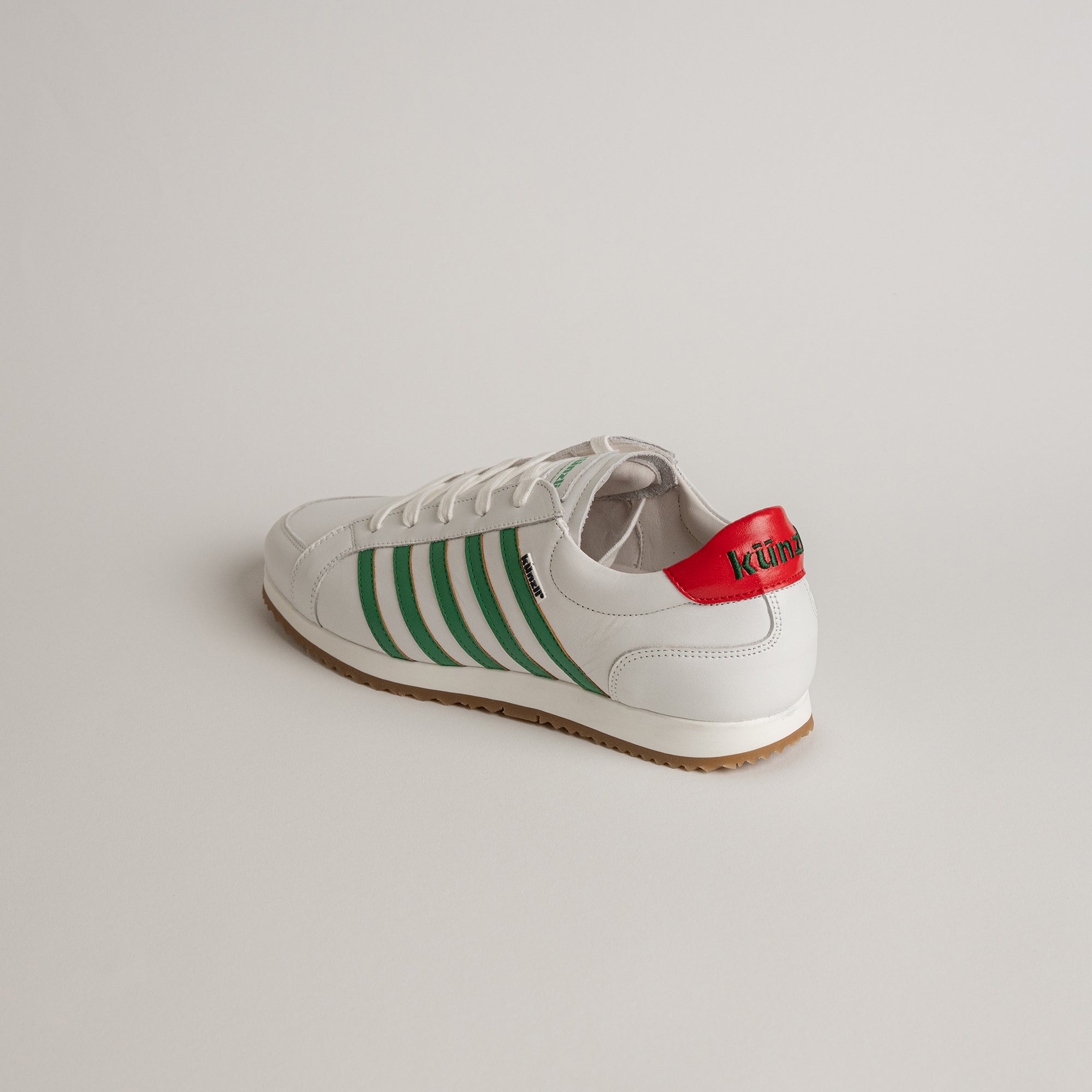 Weißer Kuenzli Schuh mit grünen Streifen und rotem Detail auf hellem Hintergrund.