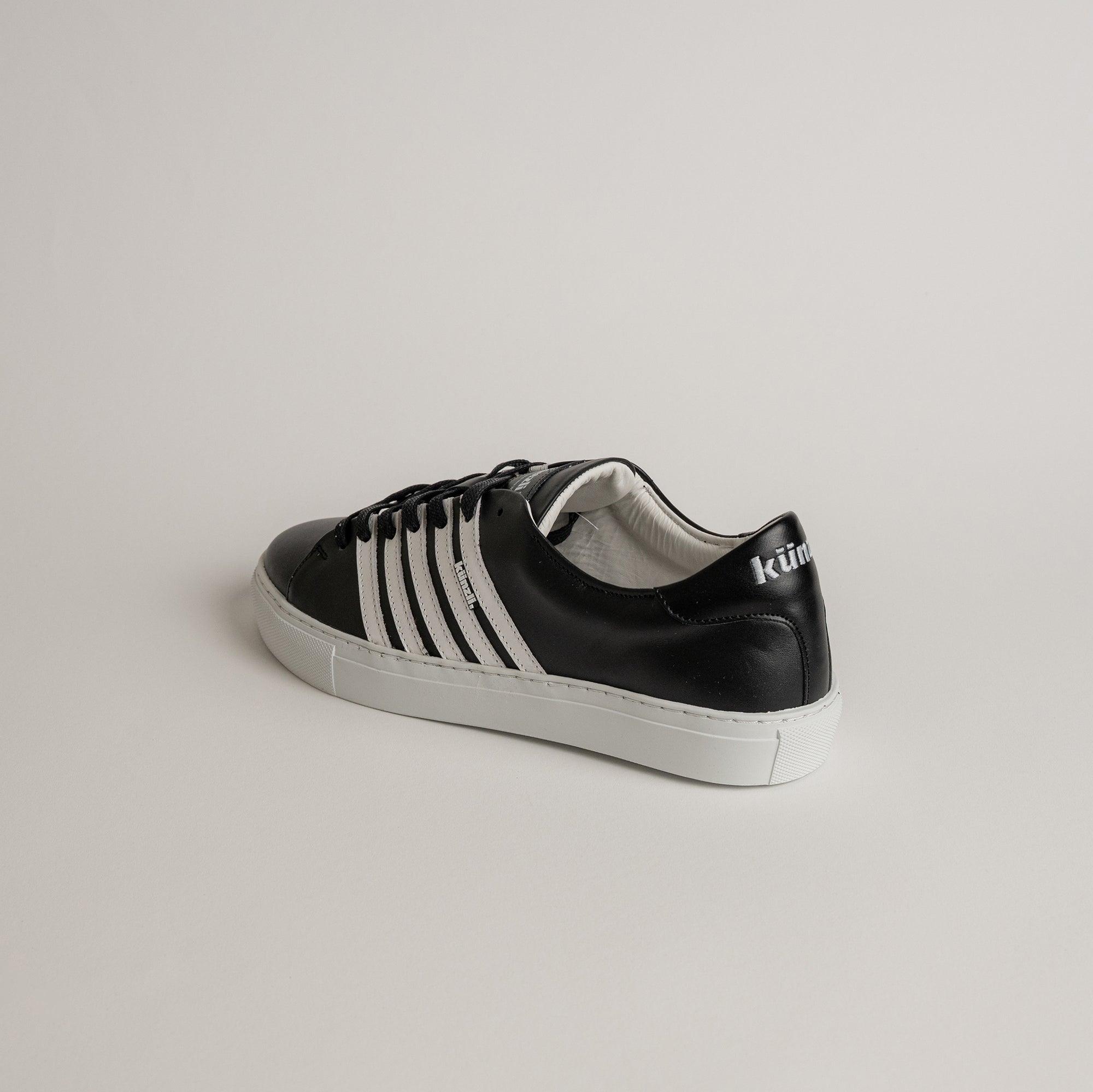 Schwarzer Kuenzli Schuh aus Leder mit weißen Streifen auf hellem Hintergrund.