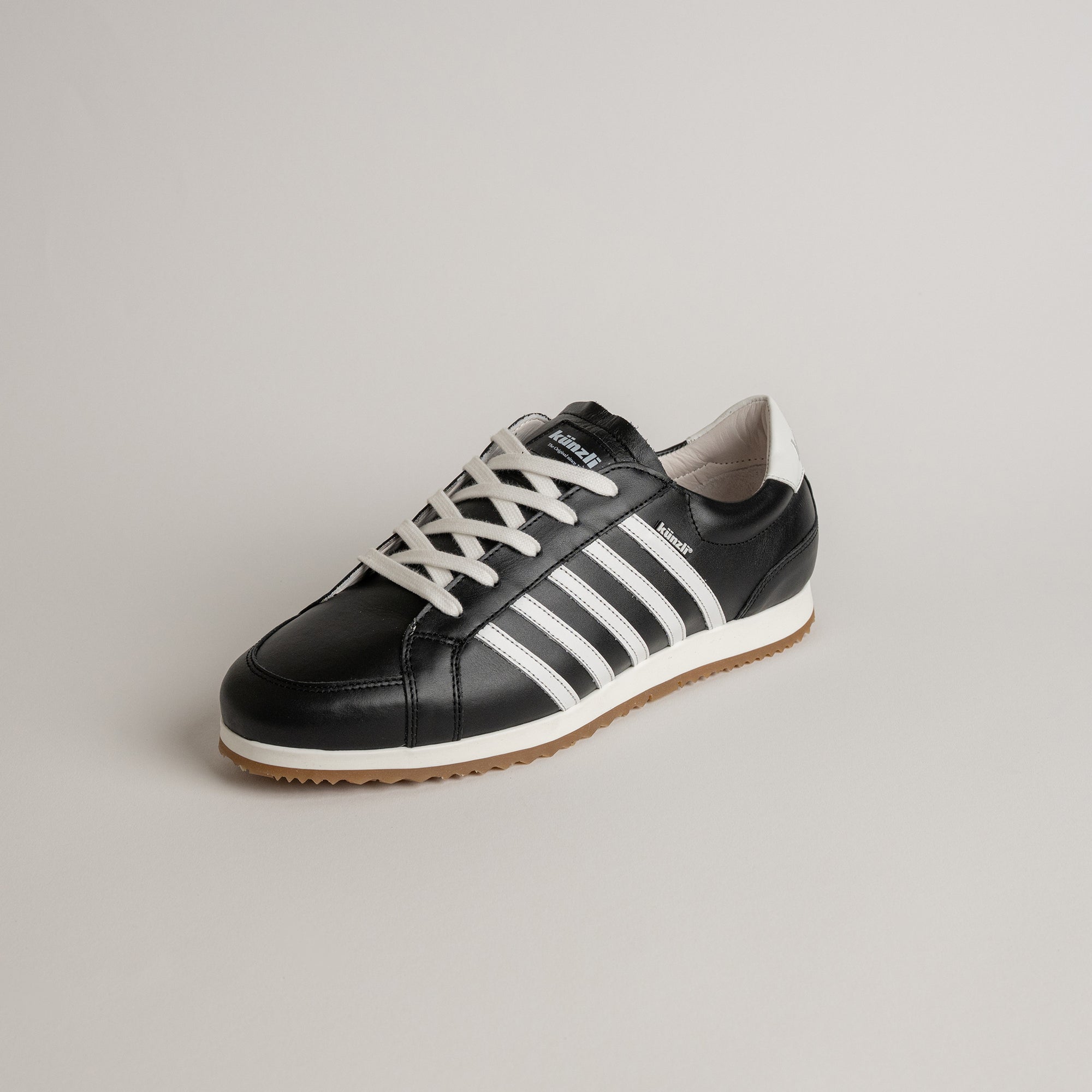 Schwarzer Kuenzli Schuh mit weißen Streifen und Schnürsenkeln auf hellem Hintergrund.