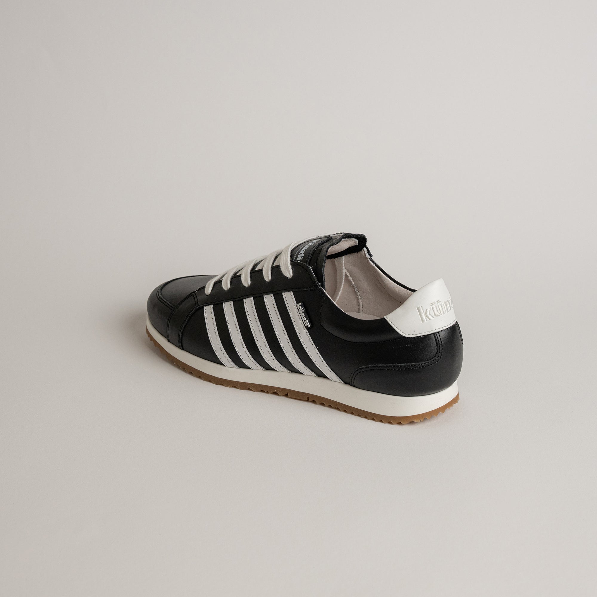 Schwarzer Kuenzli Schuh mit weißen Streifen und Schnürsenkeln auf hellem Hintergrund.