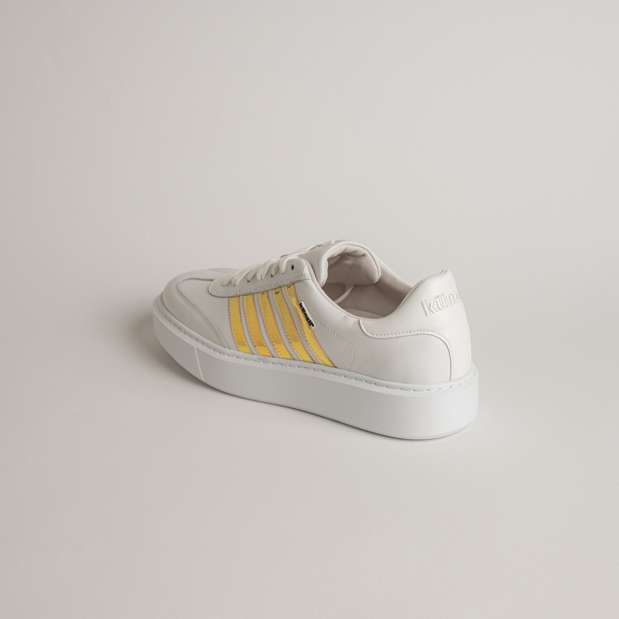 Weißer Kuenzli Schuh mit gelben Streifen auf hellem Hintergrund.