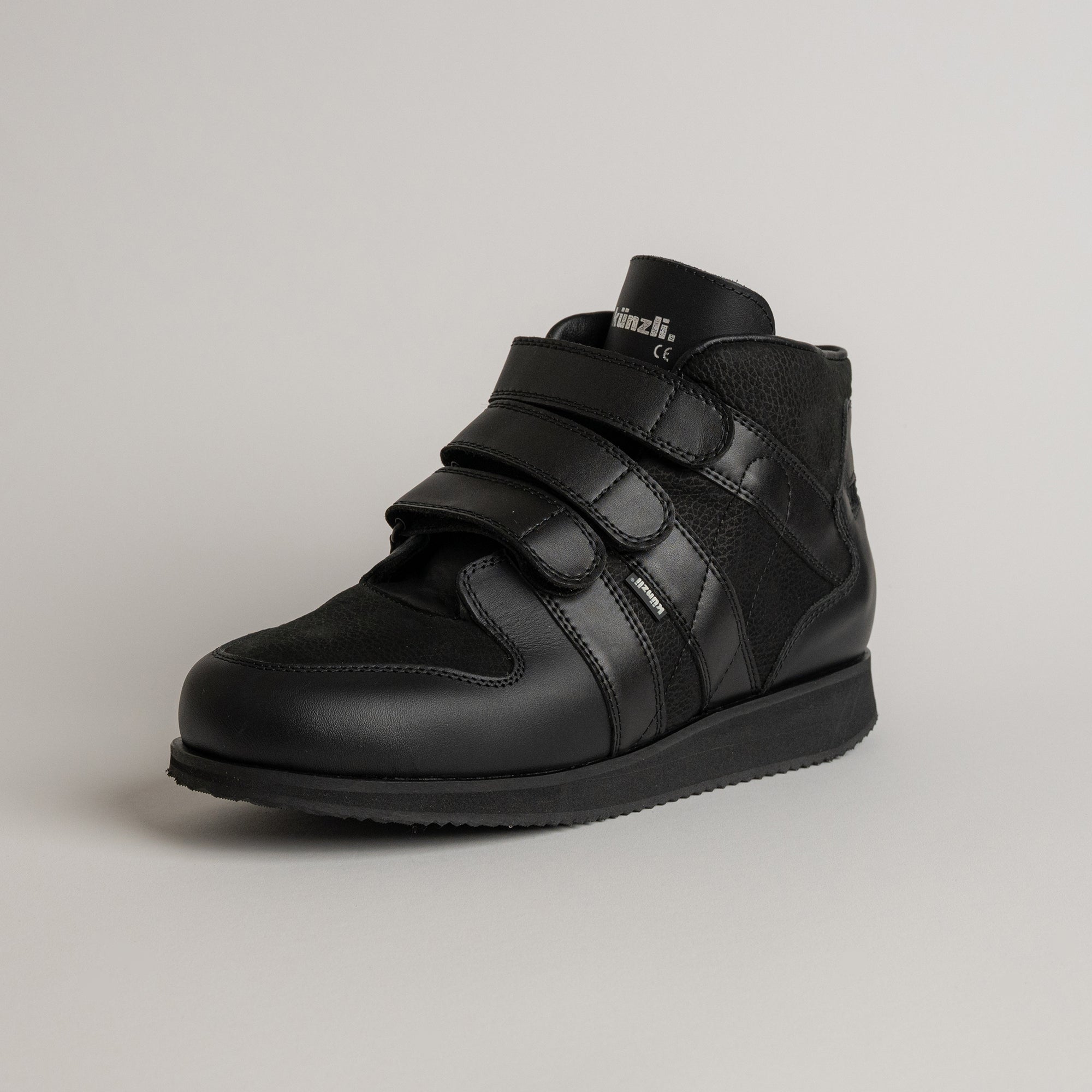 Schwarzer Kuenzli Schuh aus Leder mit Klettverschluss auf grauem Hintergrund.