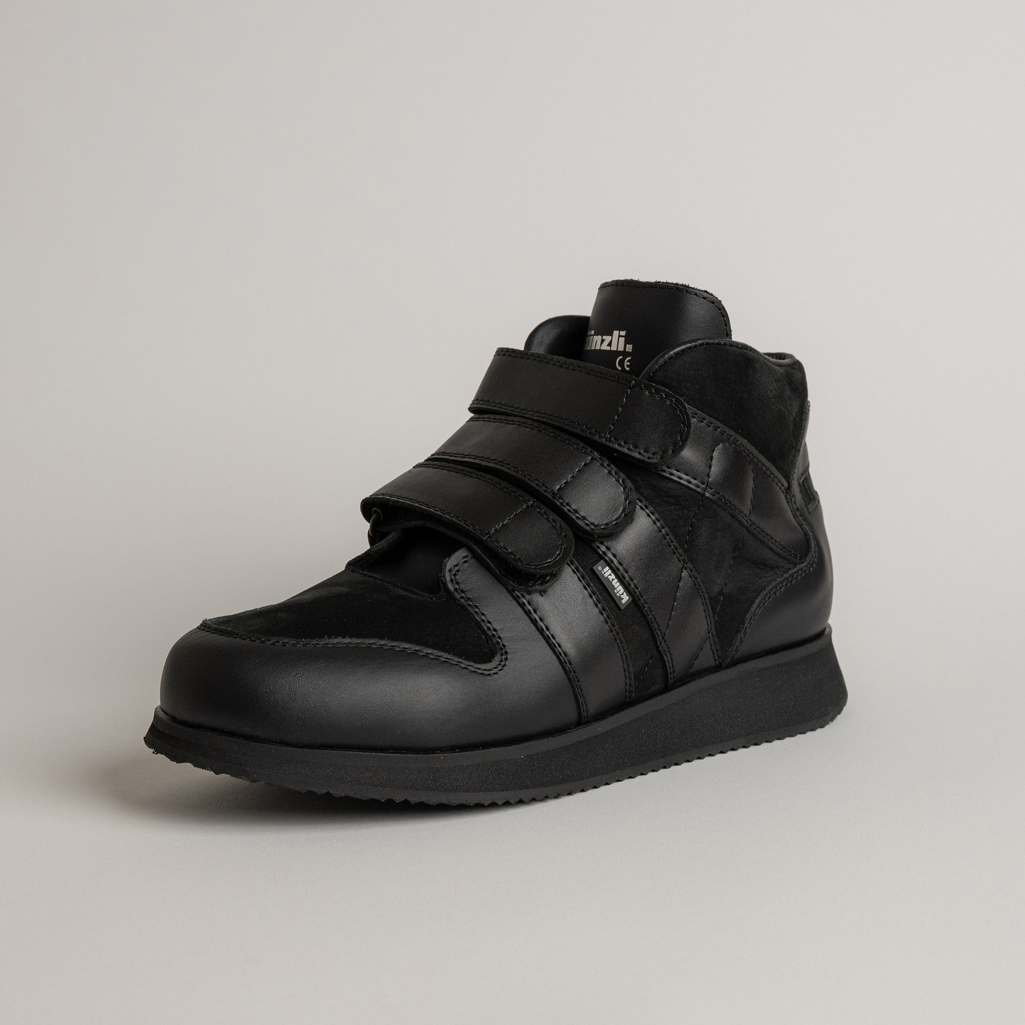 Schwarzer Lederschuh von Kuenzli Schuhe mit Klettverschluss auf grauem Hintergrund.