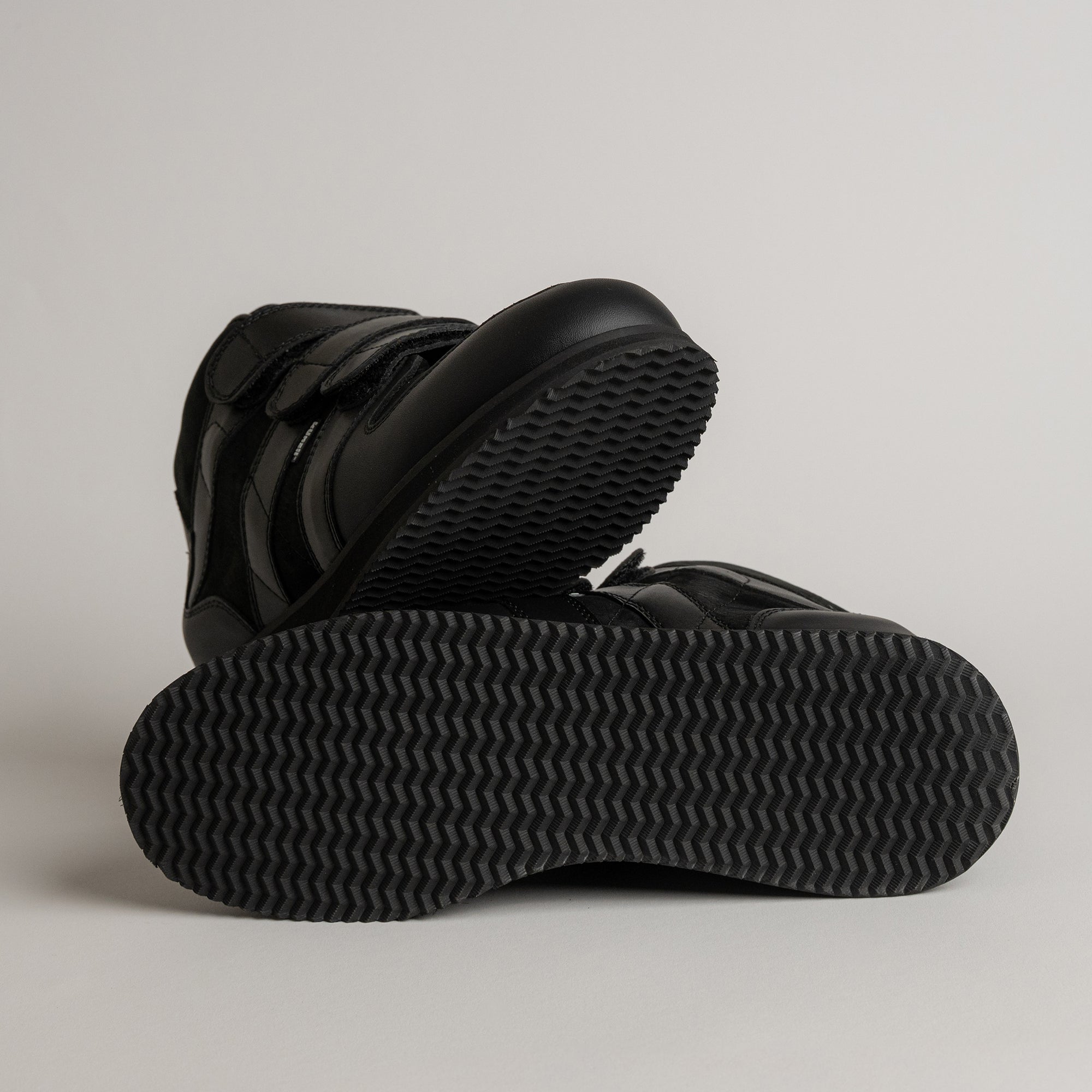 Schwarze Kuenzli Schuhe mit rutschfester Sohle auf grauem Hintergrund präsentiert.