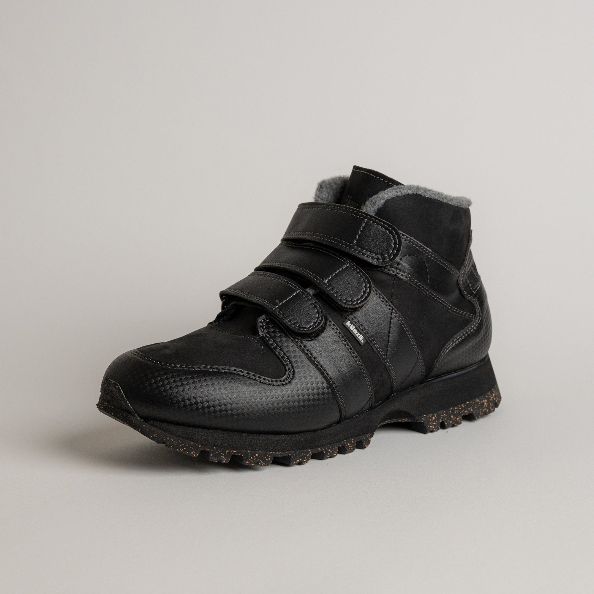 Schwarzer Kuenzli Schuhe Winterstiefel mit Klettverschluss und robustem Profil auf grauem Hintergrund.
