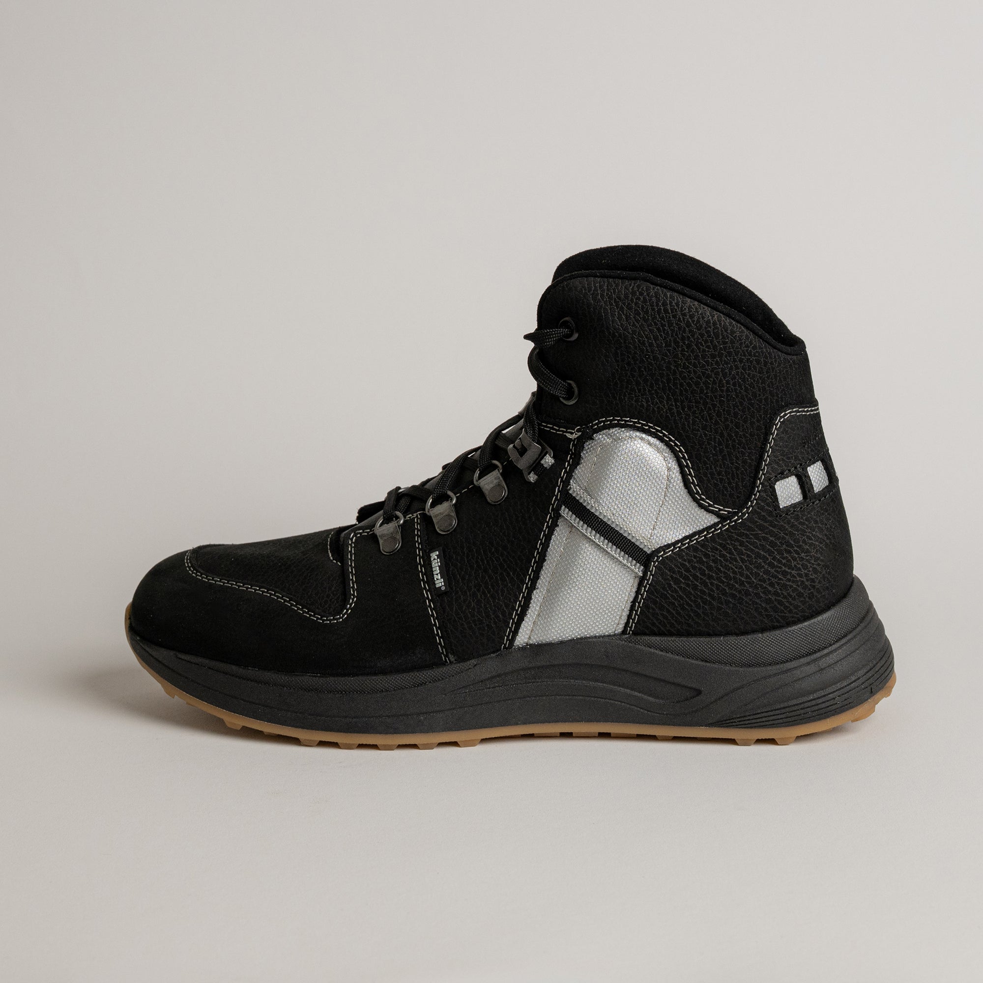 Schwarzer Kuenzli Schuhe Wanderschuh aus Leder mit reflektierenden Details auf hellem Hintergrund.