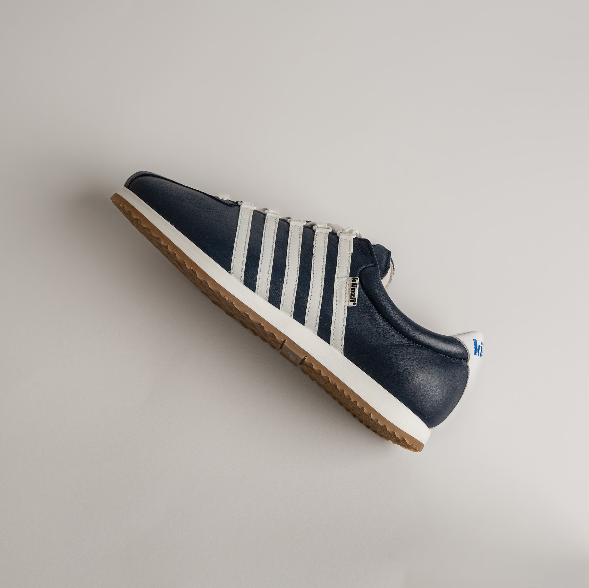 Ein blauer Kuenzli Schuh mit weißen Streifen auf hellem Hintergrund.