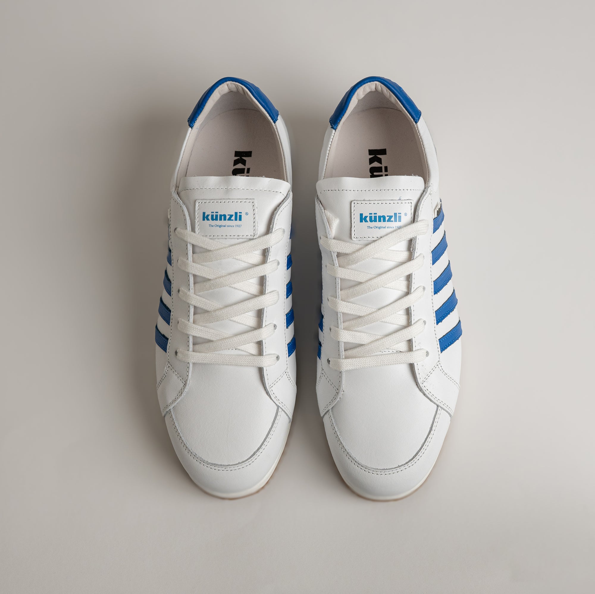 Weiße Kuenzli Schuhe mit blauen Streifen auf hellem Hintergrund, sportlich und modern.