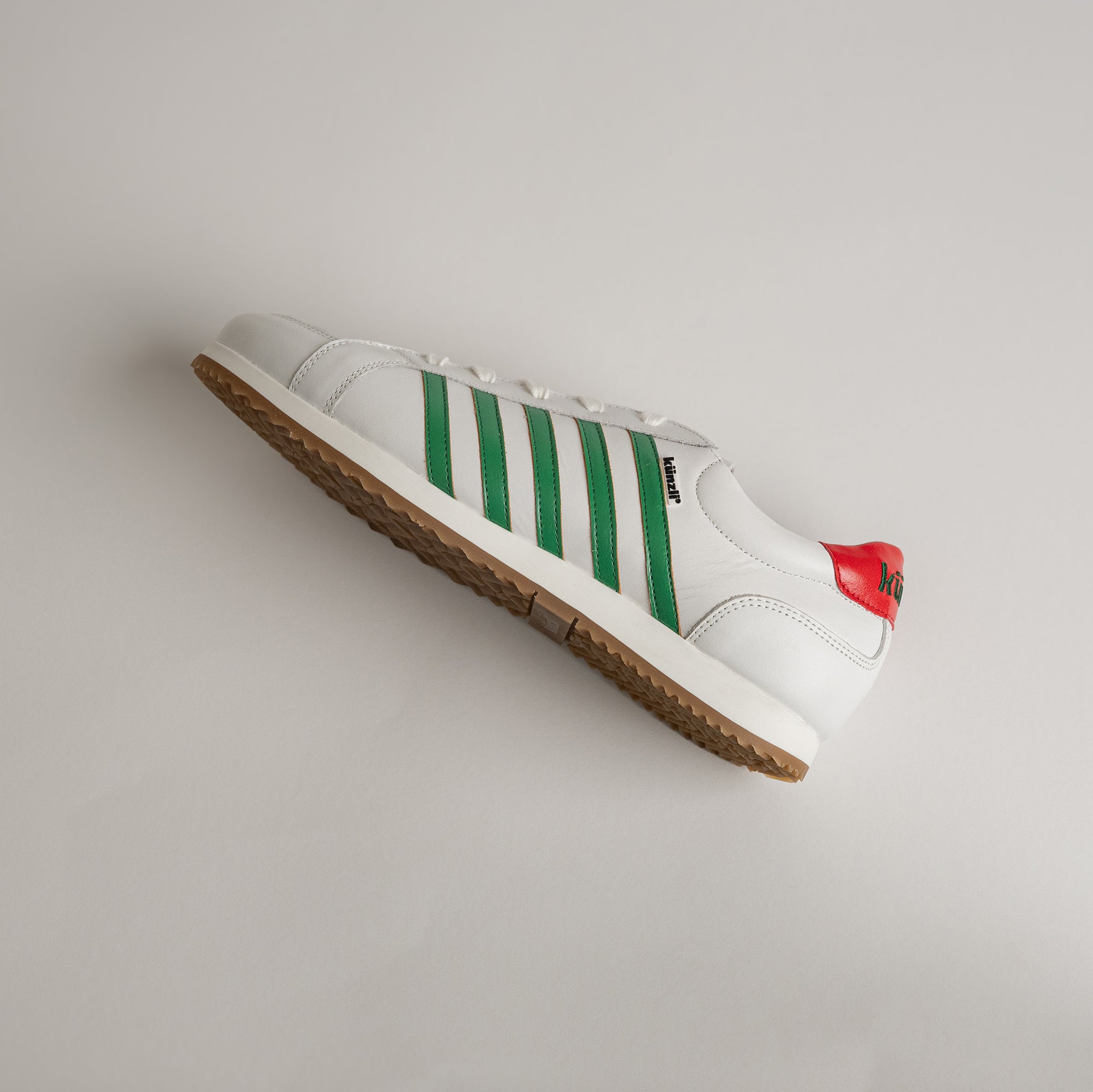 Weißer Kuenzli Schuh mit grünen Streifen und rotem Detail auf hellem Hintergrund.