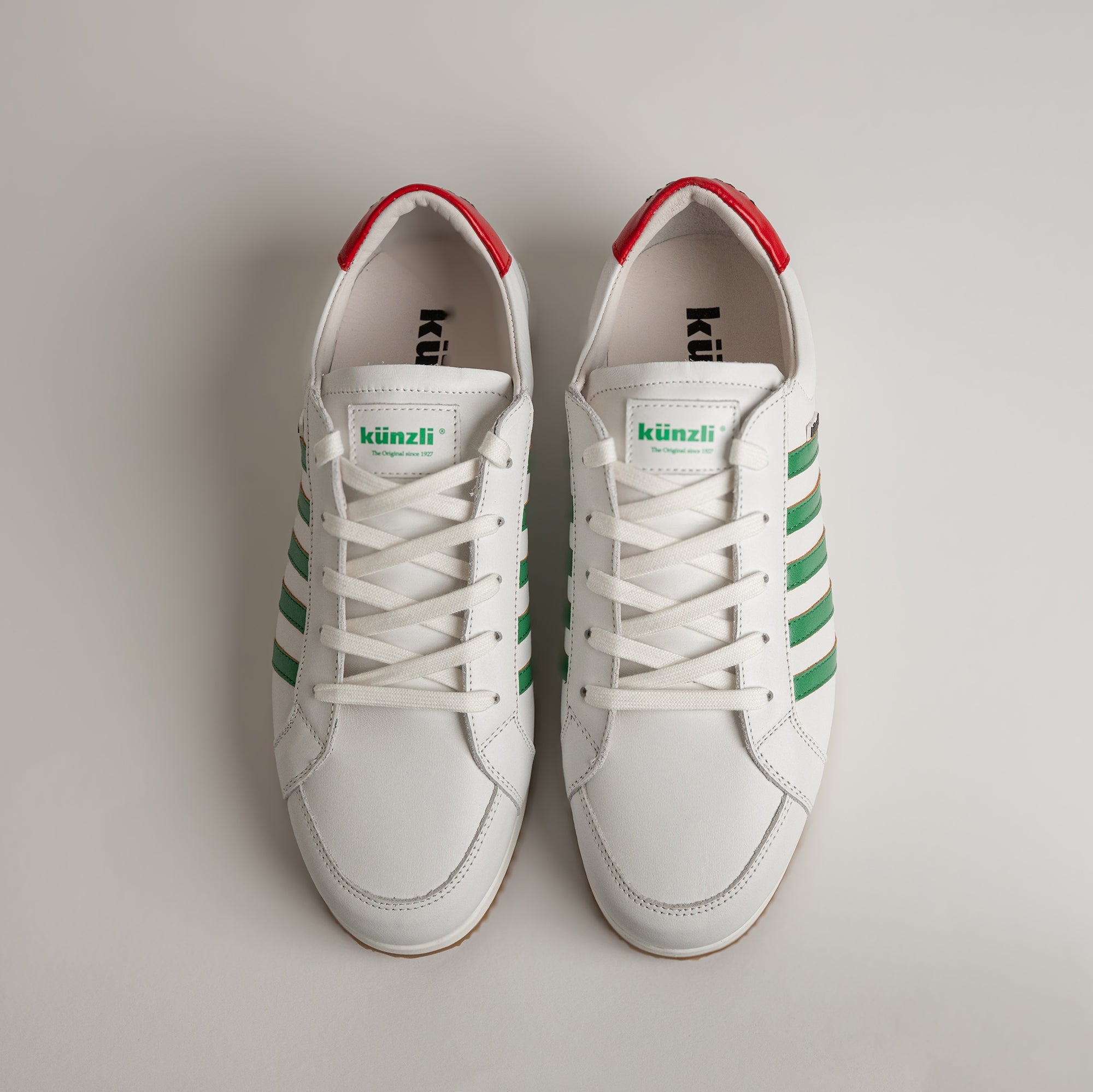 Weiße Kuenzli Schuhe mit grünen Streifen und roten Akzenten auf hellem Hintergrund.