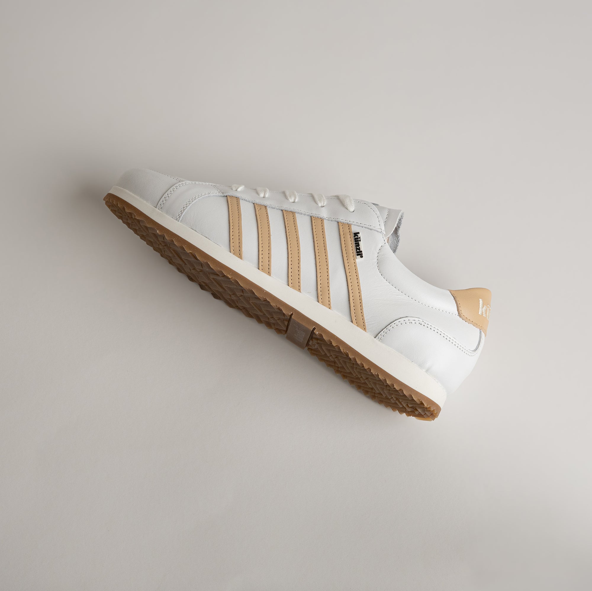 Ein weißer Kuenzli Schuh mit beigen Streifen auf hellem Hintergrund.