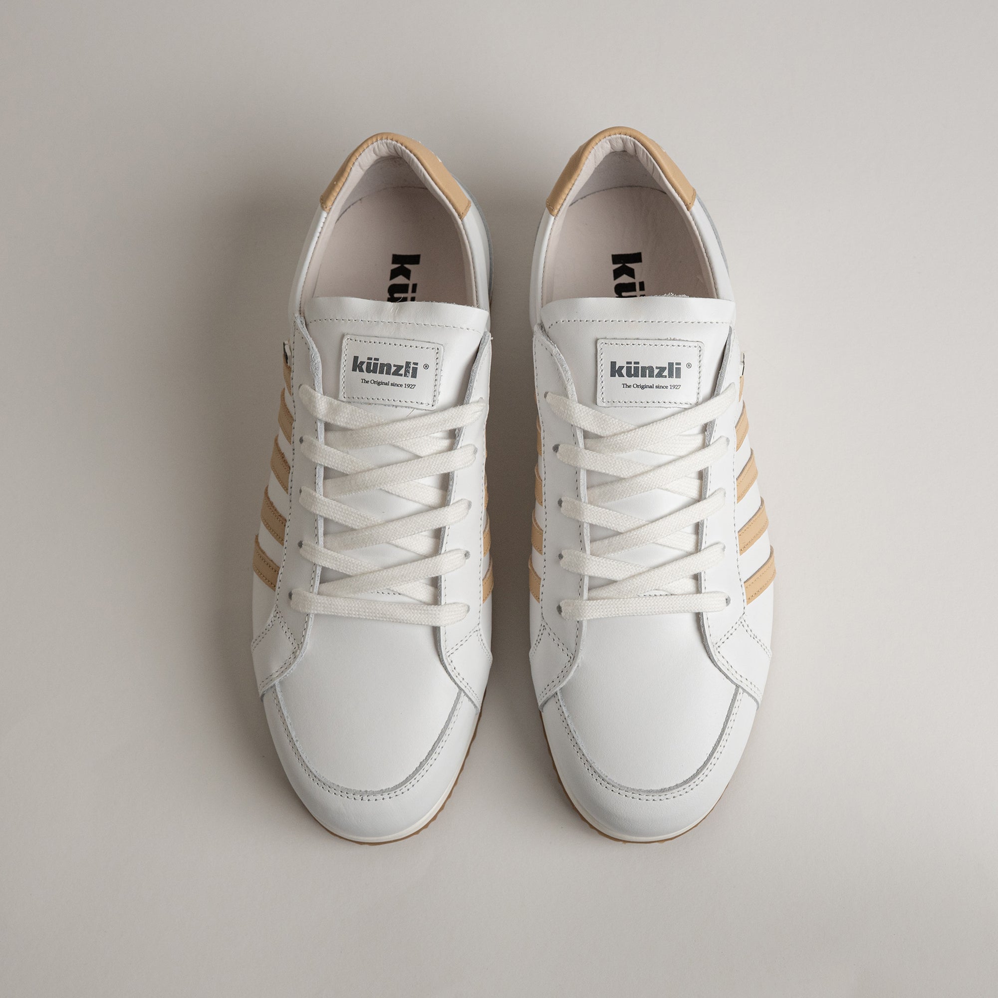 Weiße Kuenzli Schuhe mit beigen Streifen, aus Leder, auf hellem Hintergrund fotografiert.