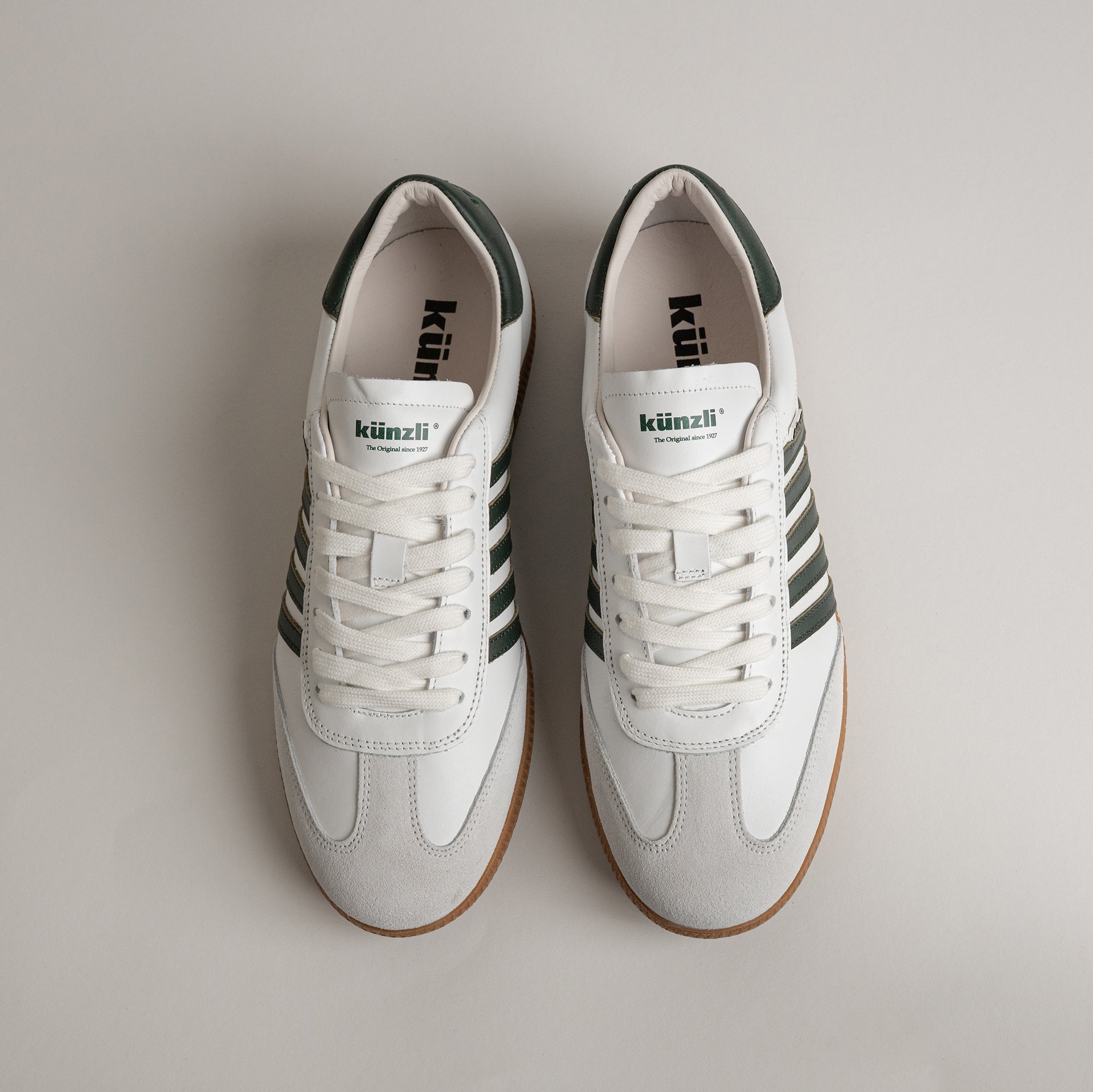 Weiße Kuenzli Schuhe mit grünen Streifen auf hellem Hintergrund, ideal für sportliche Aktivitäten.