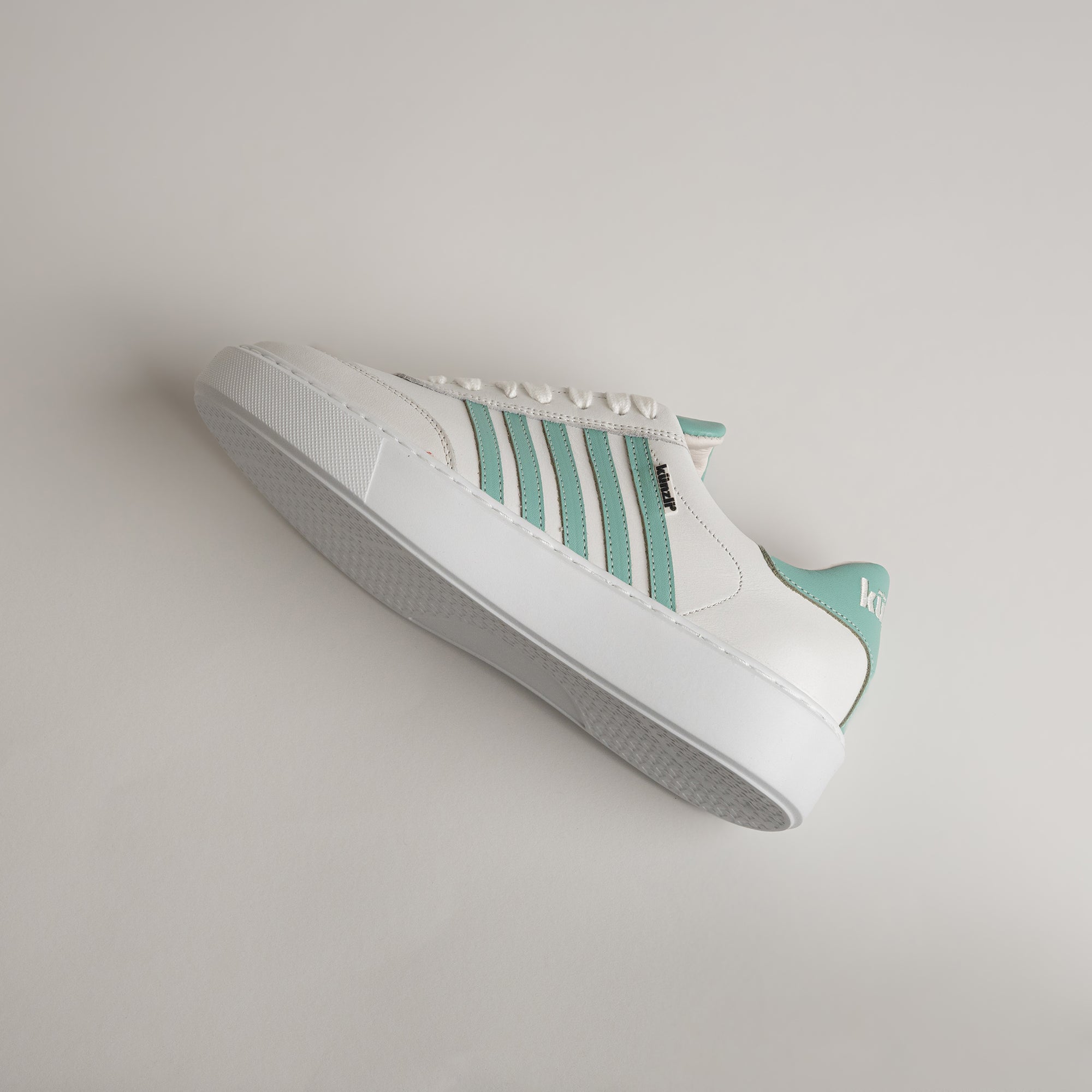 Weißer Sneaker mit grünen Streifen von Kuenzli Schuhe auf hellem Hintergrund.