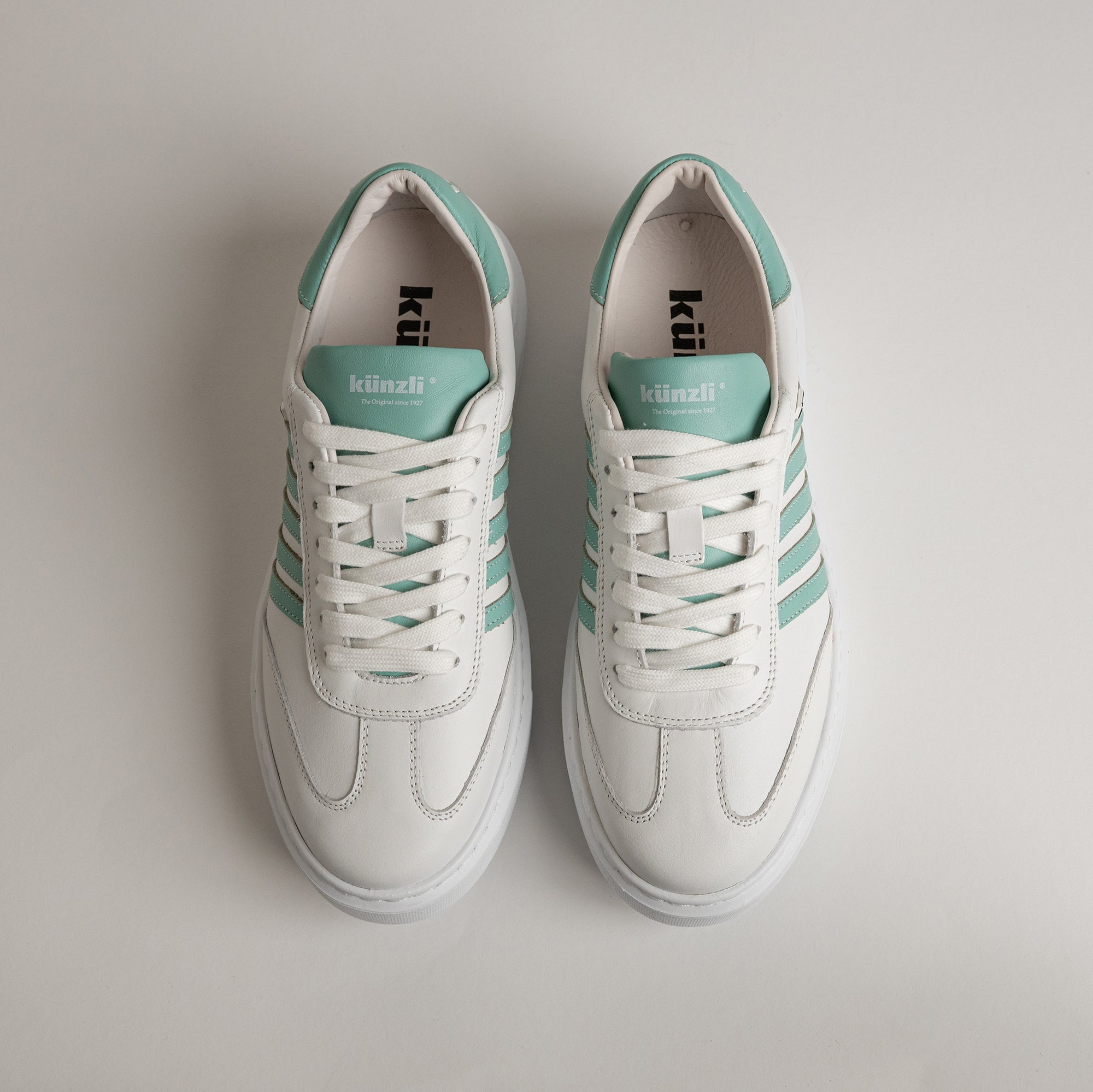 Weiße Kuenzli Schuhe mit mintgrünen Streifen auf weißem Hintergrund.