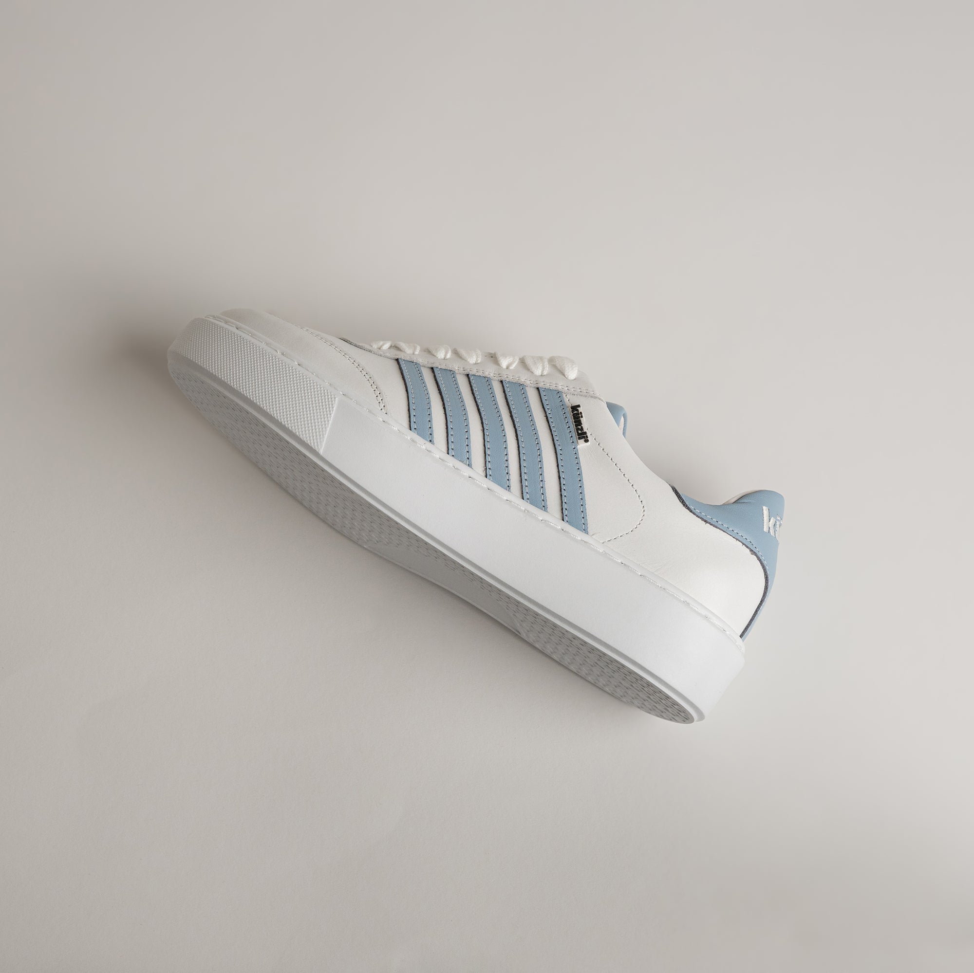 Weißer Sneaker mit blauen Streifen von Kuenzli Schuhe auf hellem Hintergrund.