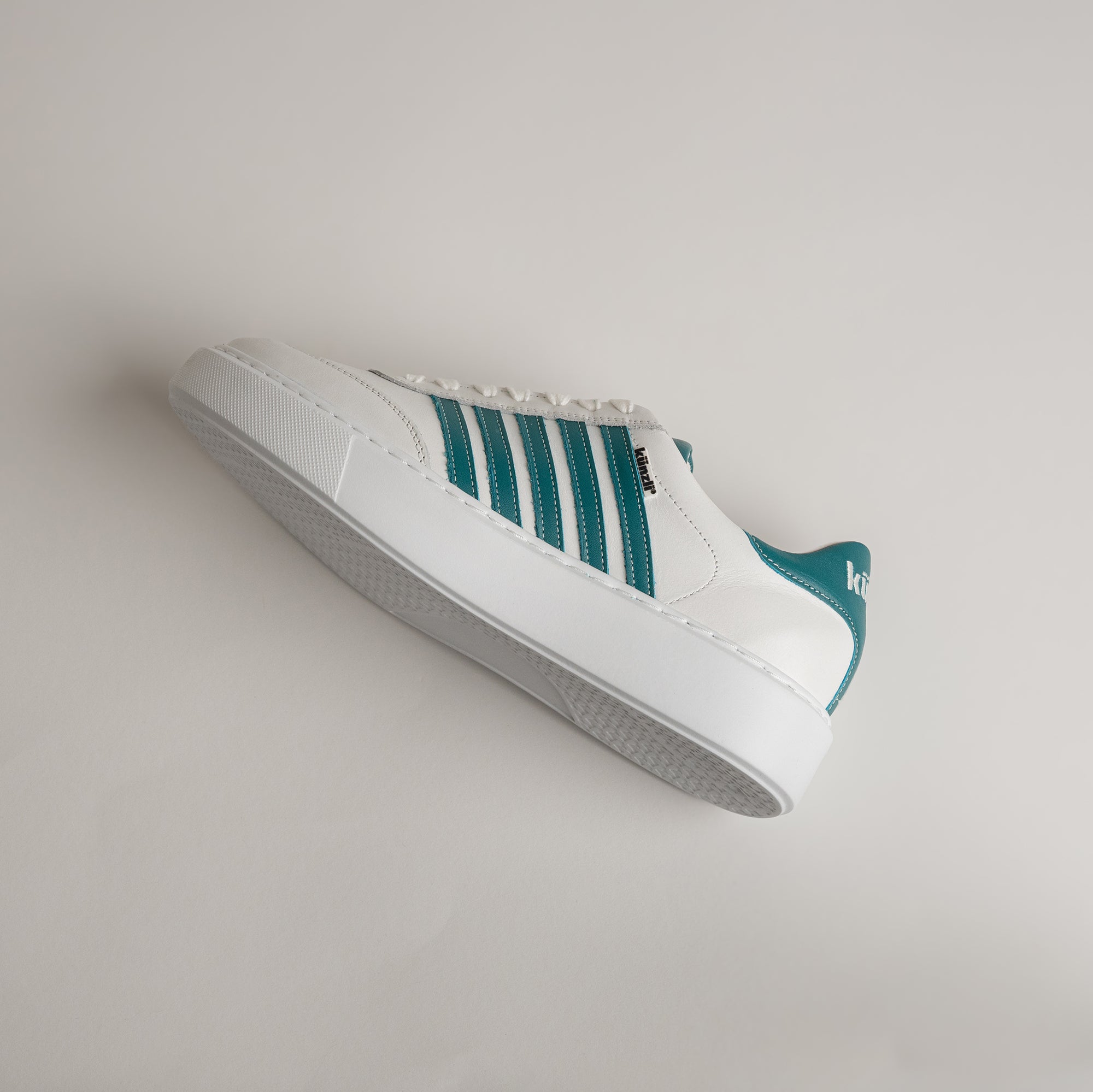 Weißer Sneaker mit grünen Streifen von Kuenzli Schuhe auf hellem Hintergrund.