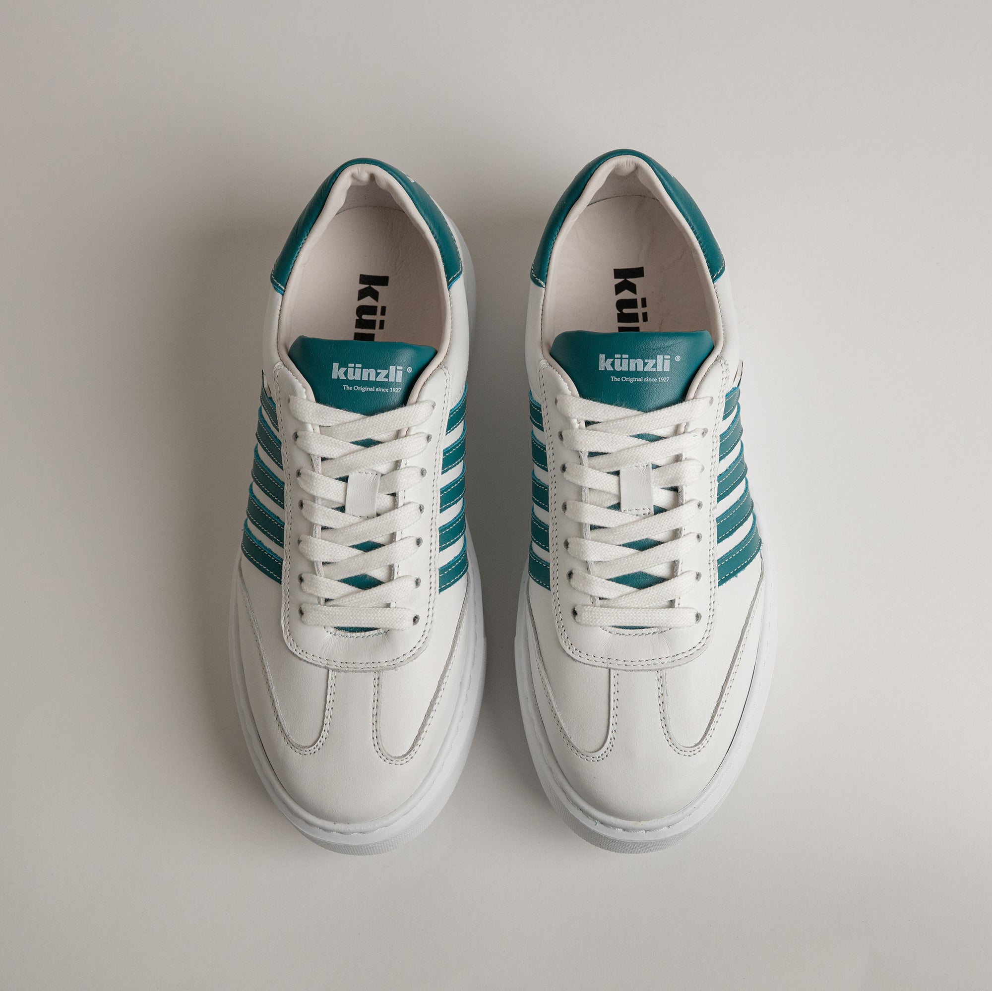 Weiße Kuenzli Schuhe mit grünen Streifen aus Leder auf hellem Hintergrund.