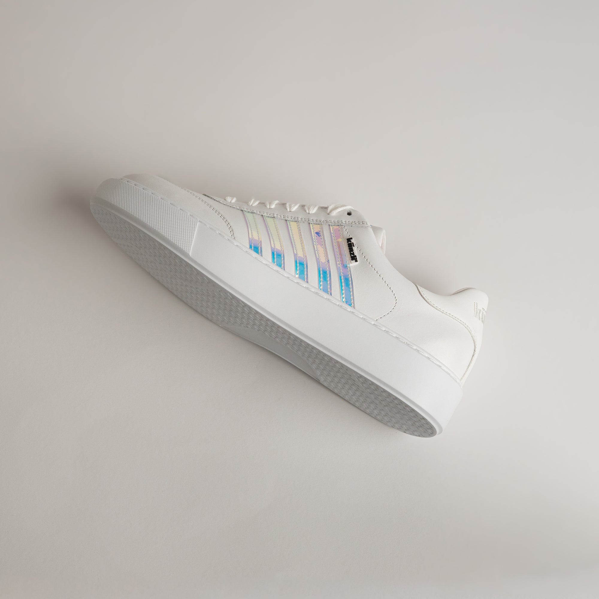 Weißer Sneaker von Kuenzli Schuhe mit schimmernden Streifen auf hellem Hintergrund.