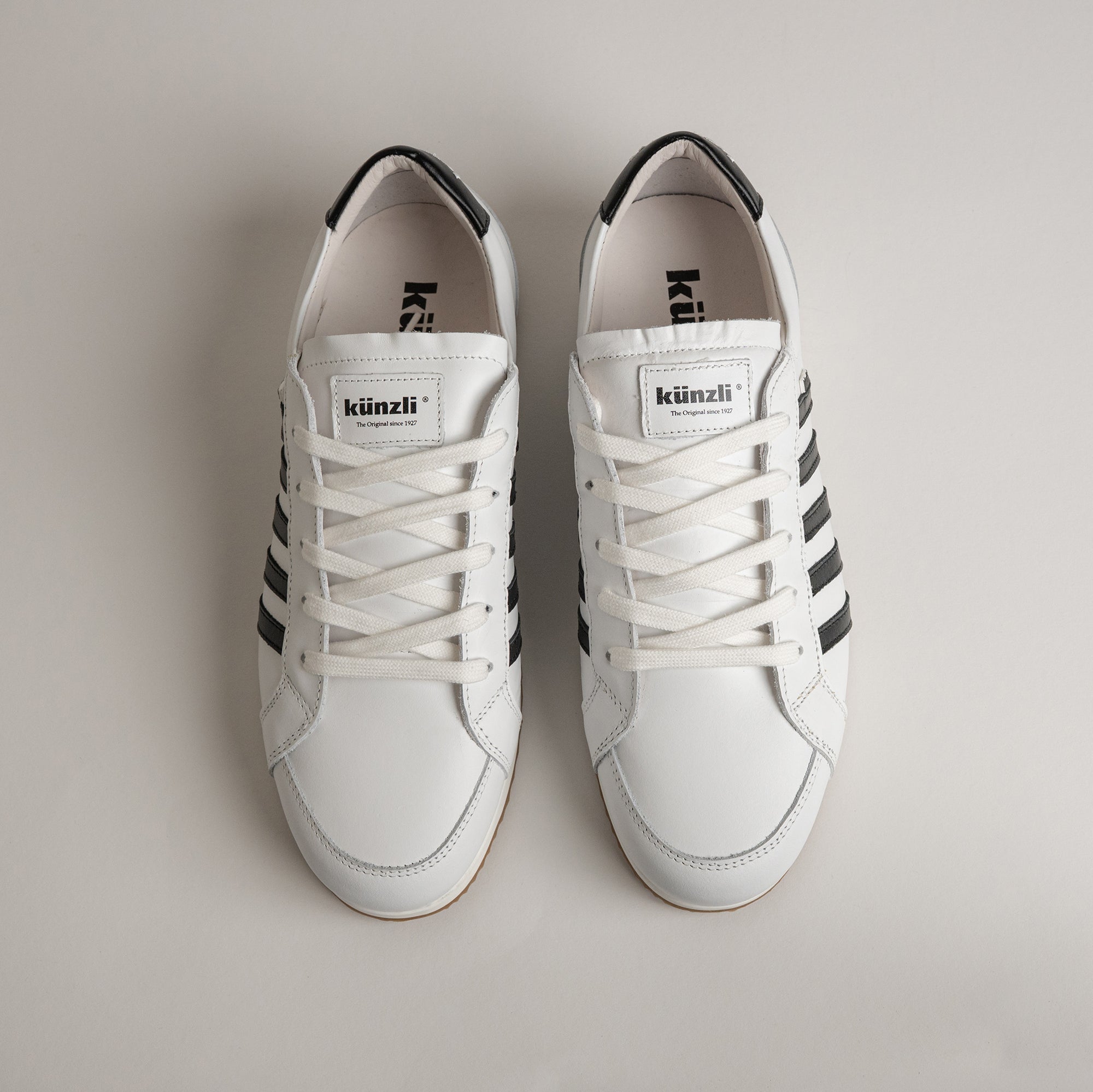 Weiße Kuenzli Schuhe mit schwarzen Streifen und Schnürsenkeln auf hellem Hintergrund.
