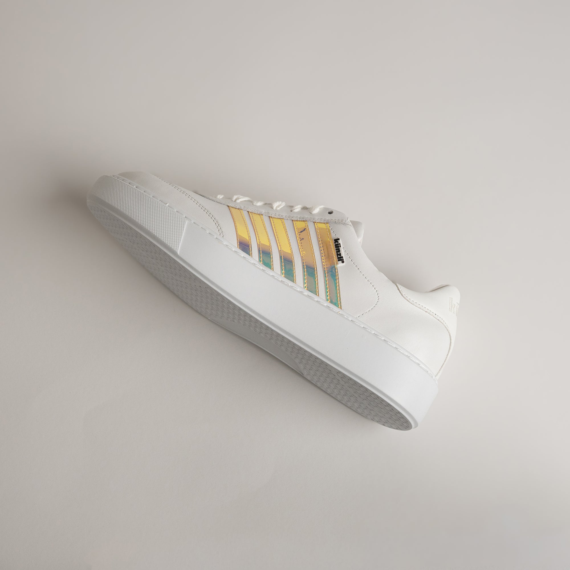 Weißer Sneaker von Kuenzli Schuhe mit schimmernden Streifen auf hellem Hintergrund.