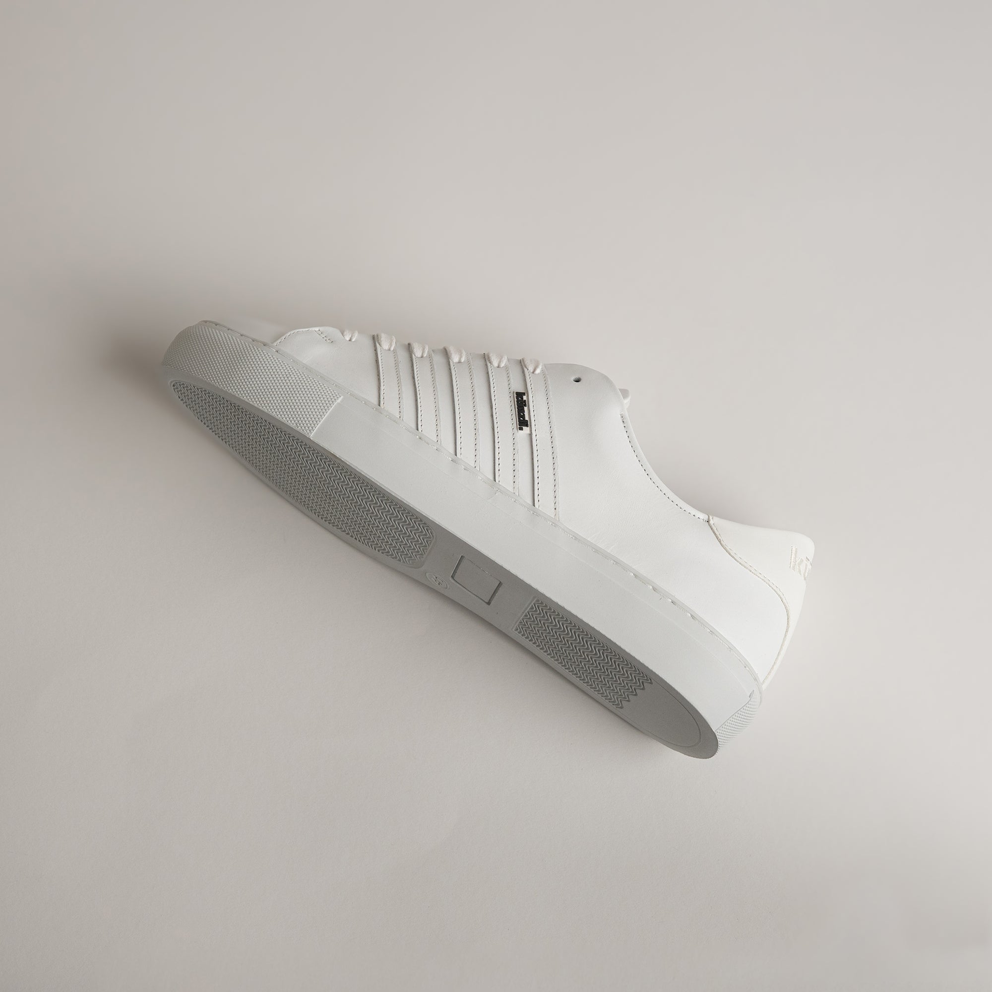 Weißer Ledersneaker von Kuenzli Schuhe mit seitlichem Logo auf hellem Hintergrund.