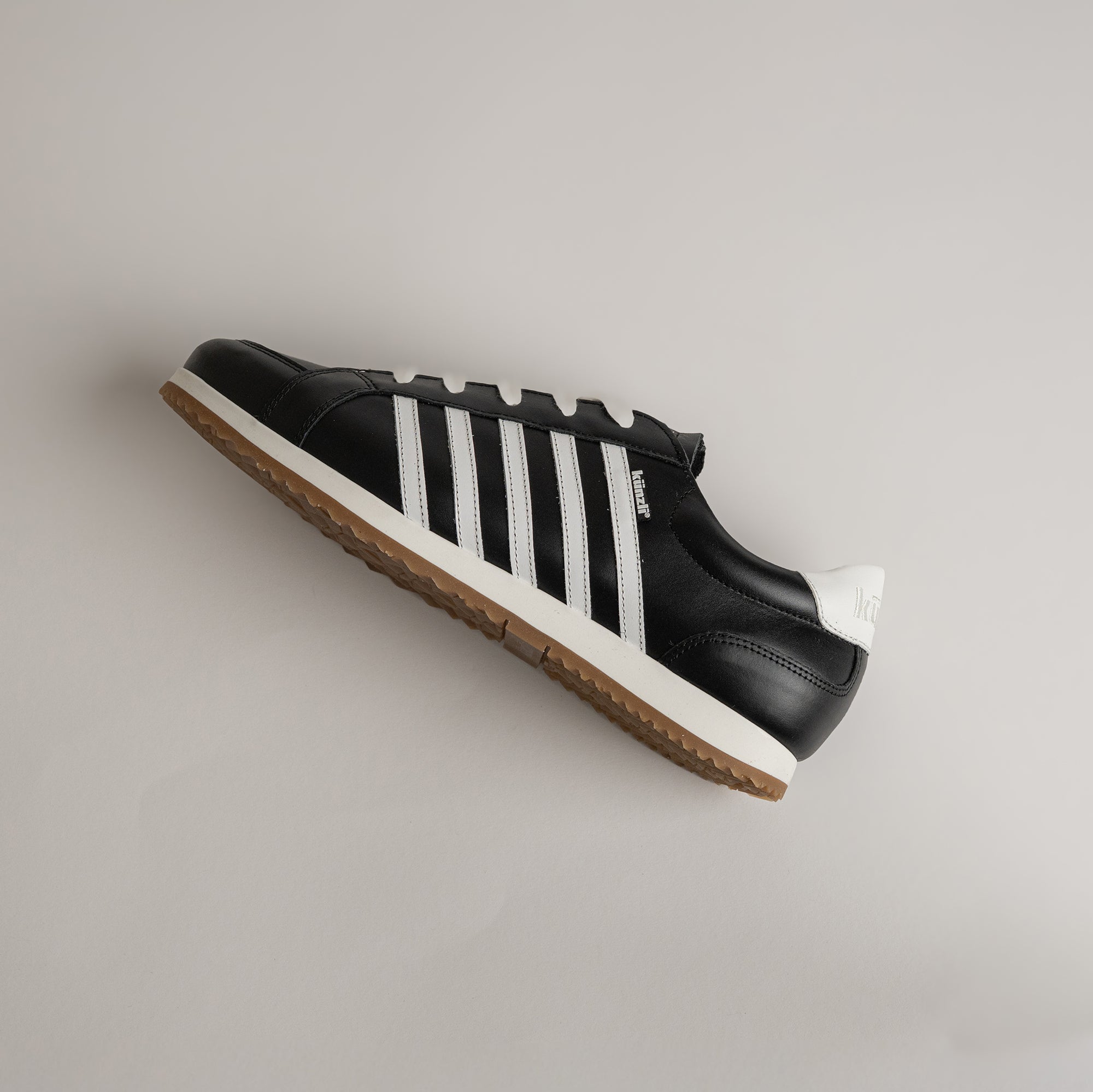 Schwarzer Kuenzli Schuh mit weißen Streifen auf hellem Hintergrund, sportlich und modern.