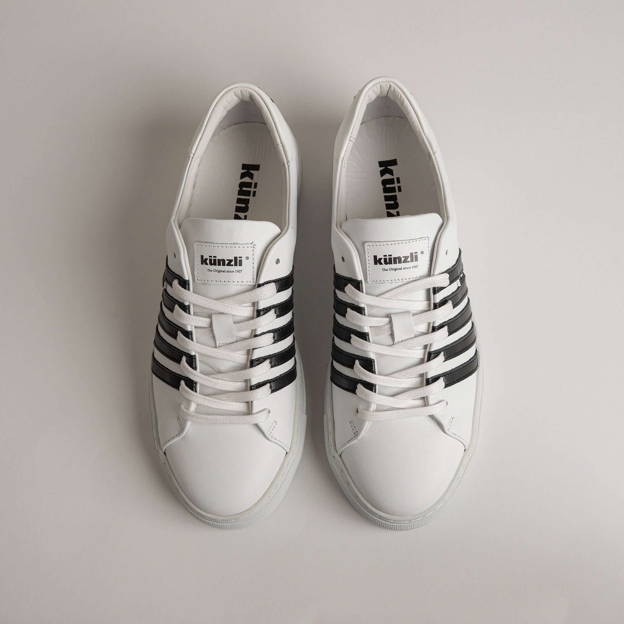 Weiße Kuenzli Schuhe mit schwarzen Streifen auf hellem Hintergrund, sportlich und modern.