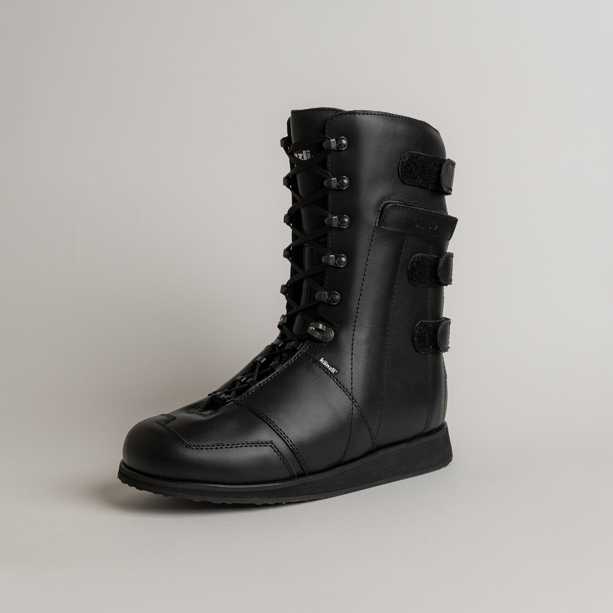 Schwarzer Lederstiefel von Kuenzli Schuhe mit Schnürung und Klettverschluss auf grauem Hintergrund.