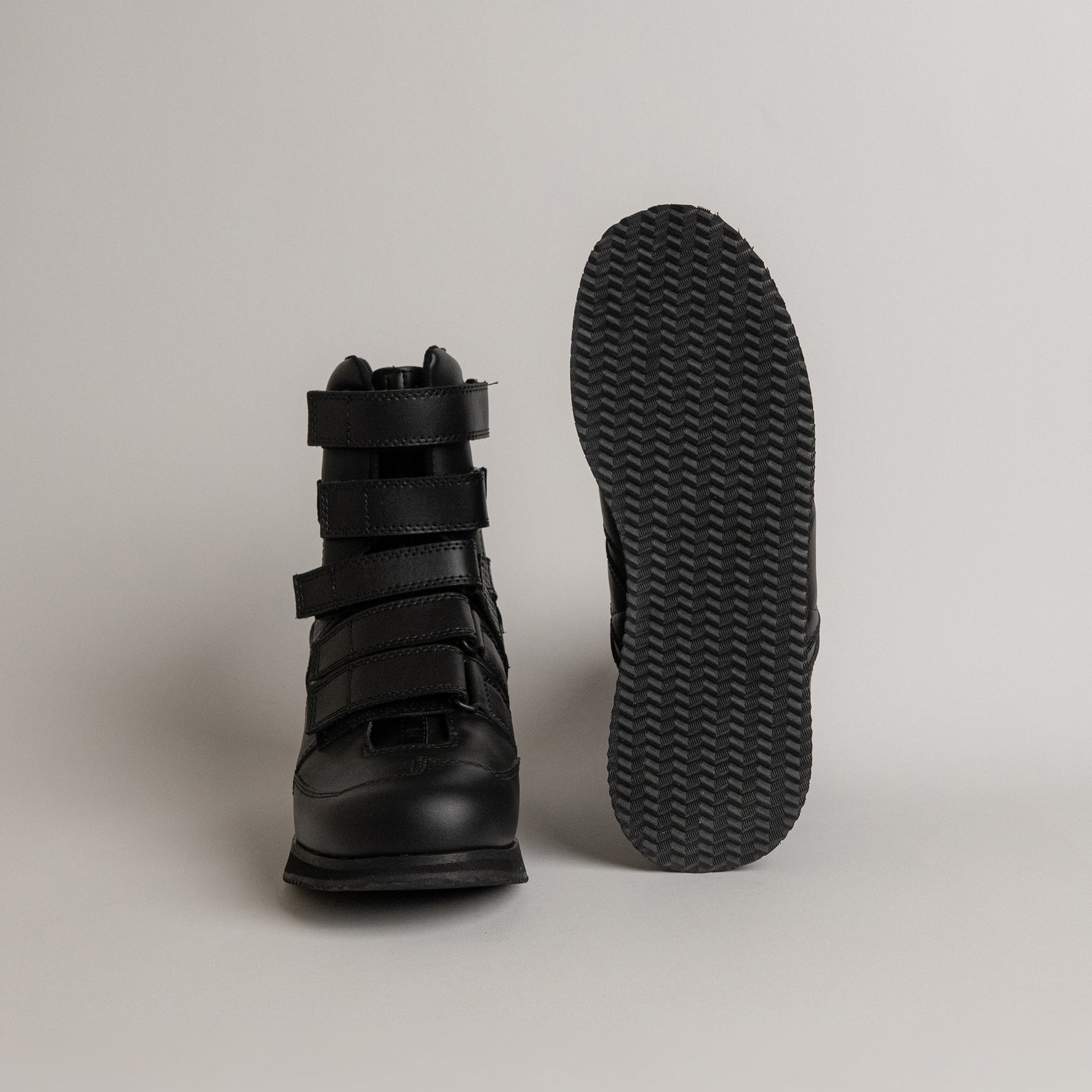 Schwarze Kuenzli Schuhe mit Klettverschluss und rutschfester Sohle auf grauem Hintergrund.