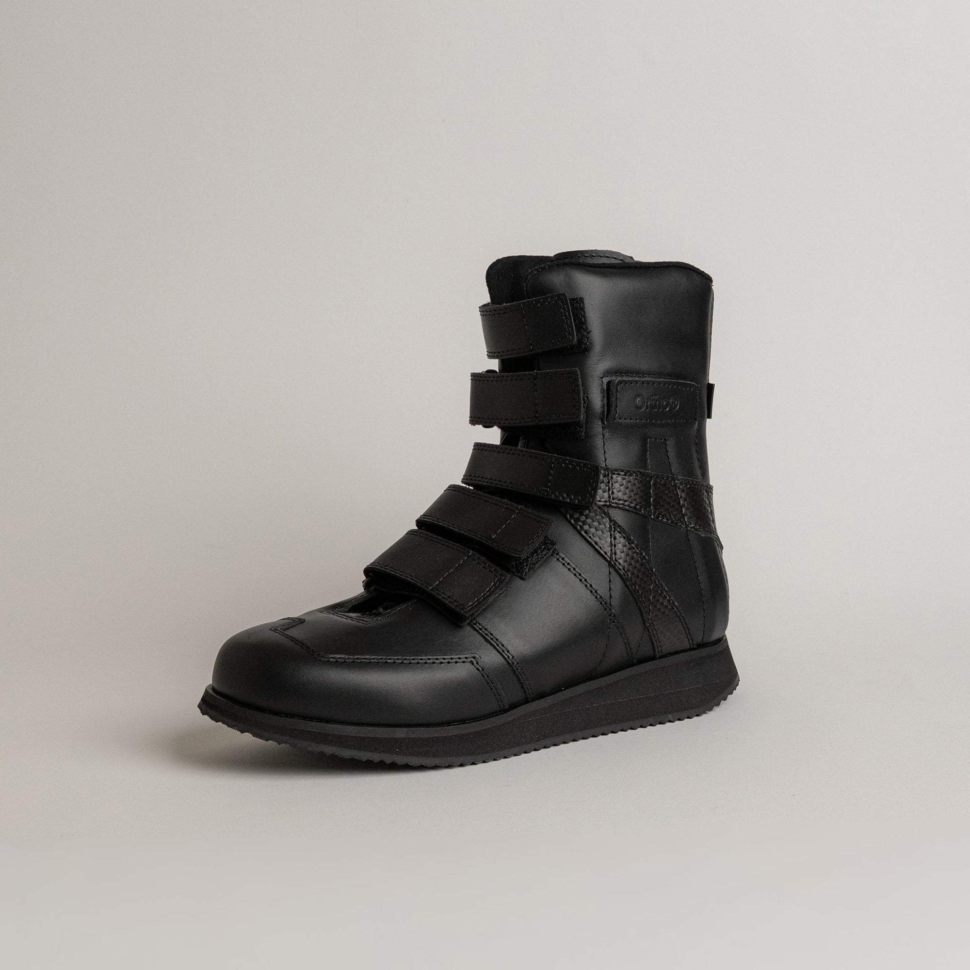 Ein schwarzer orthopädischer Schuh von Kuenzli Schuhe mit Klettverschlüssen auf grauem Hintergrund.