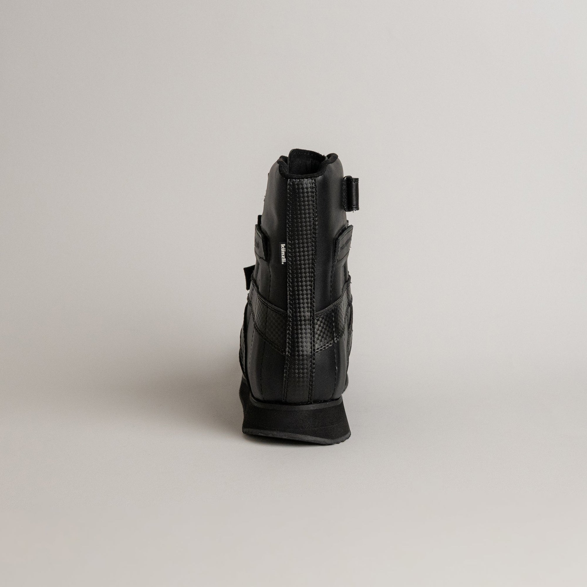 Schwarzer orthopädischer Schuh von Kuenzli Schuhe mit Klettverschluss auf grauem Hintergrund.