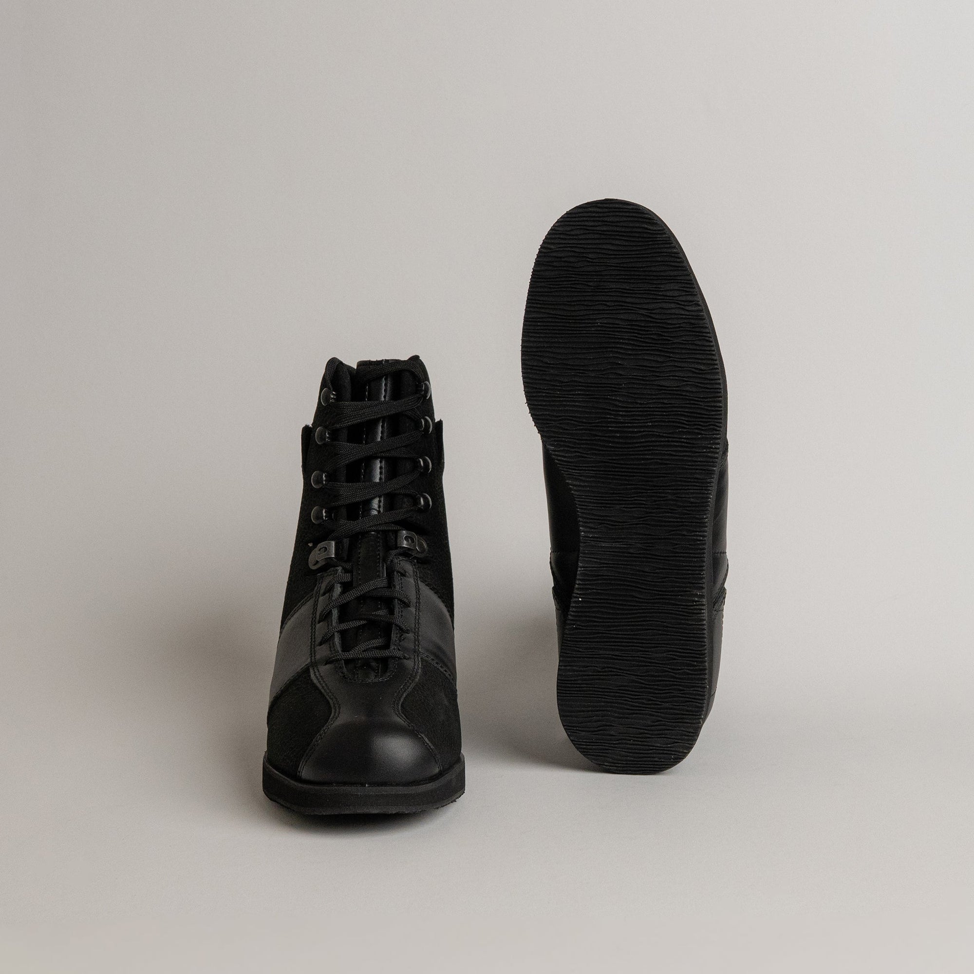 Schwarze Kuenzli Schuhe aus Leder, seitlich und von unten gezeigt, auf grauem Hintergrund.