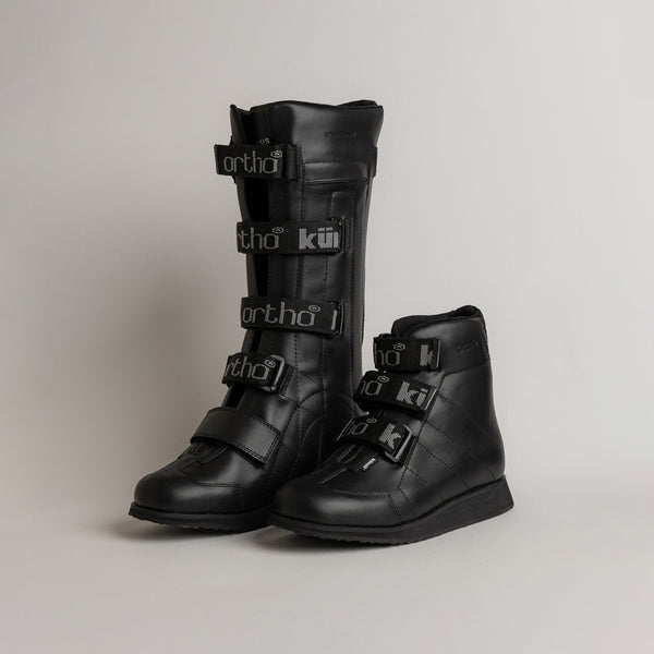 Schwarze orthopädische Stiefel von Kuenzli Schuhe mit Klettverschlüssen auf grauem Hintergrund.