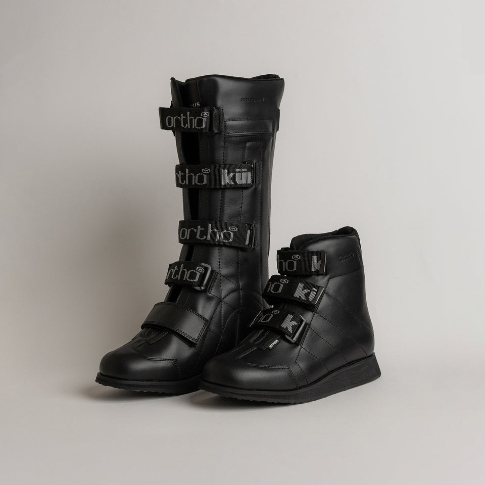 Schwarze orthopädische Stiefel von Kuenzli Schuhe mit Klettverschlüssen auf grauem Hintergrund.