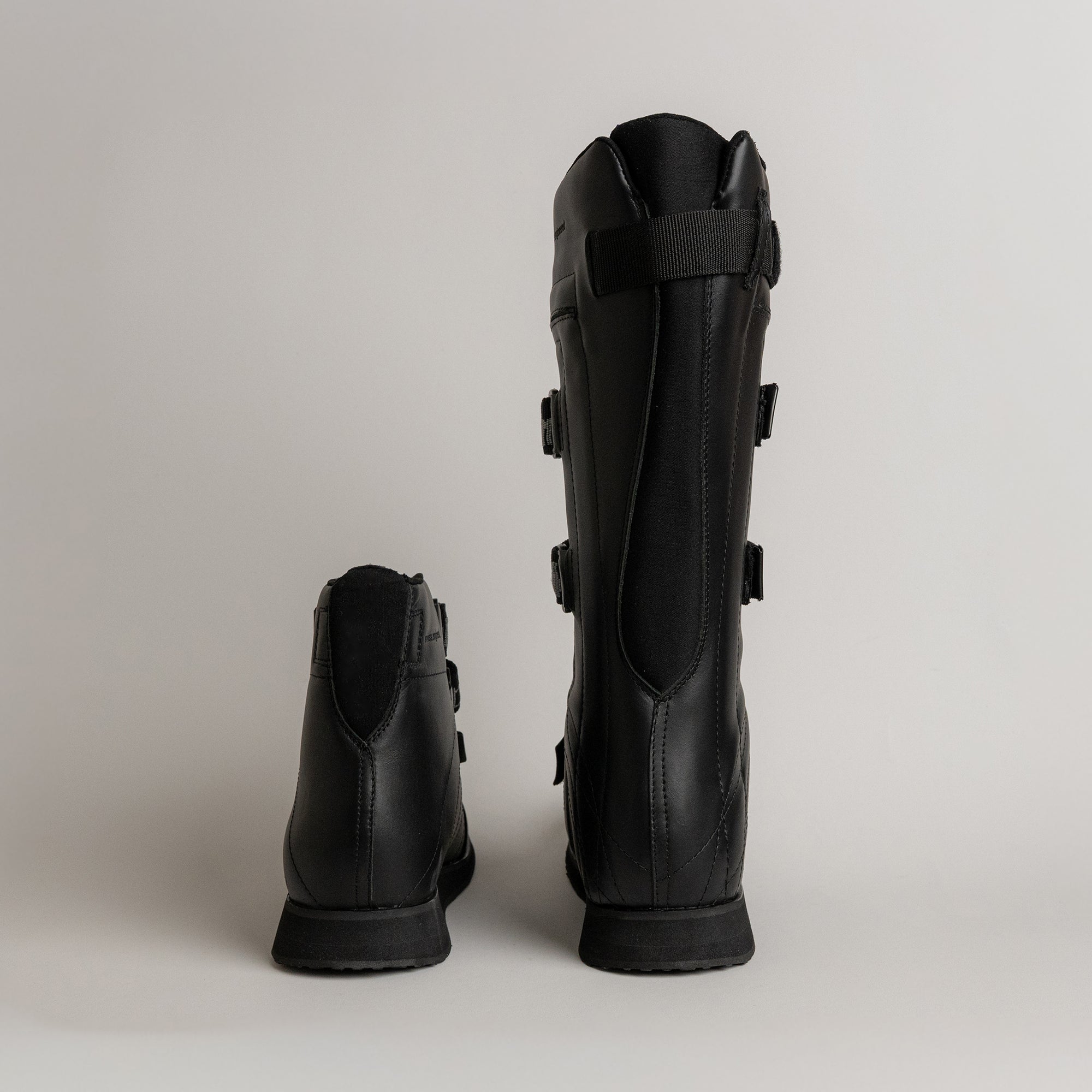 Zwei schwarze Lederstiefel von Kuenzli Schuhe, nebeneinander auf grauem Hintergrund.