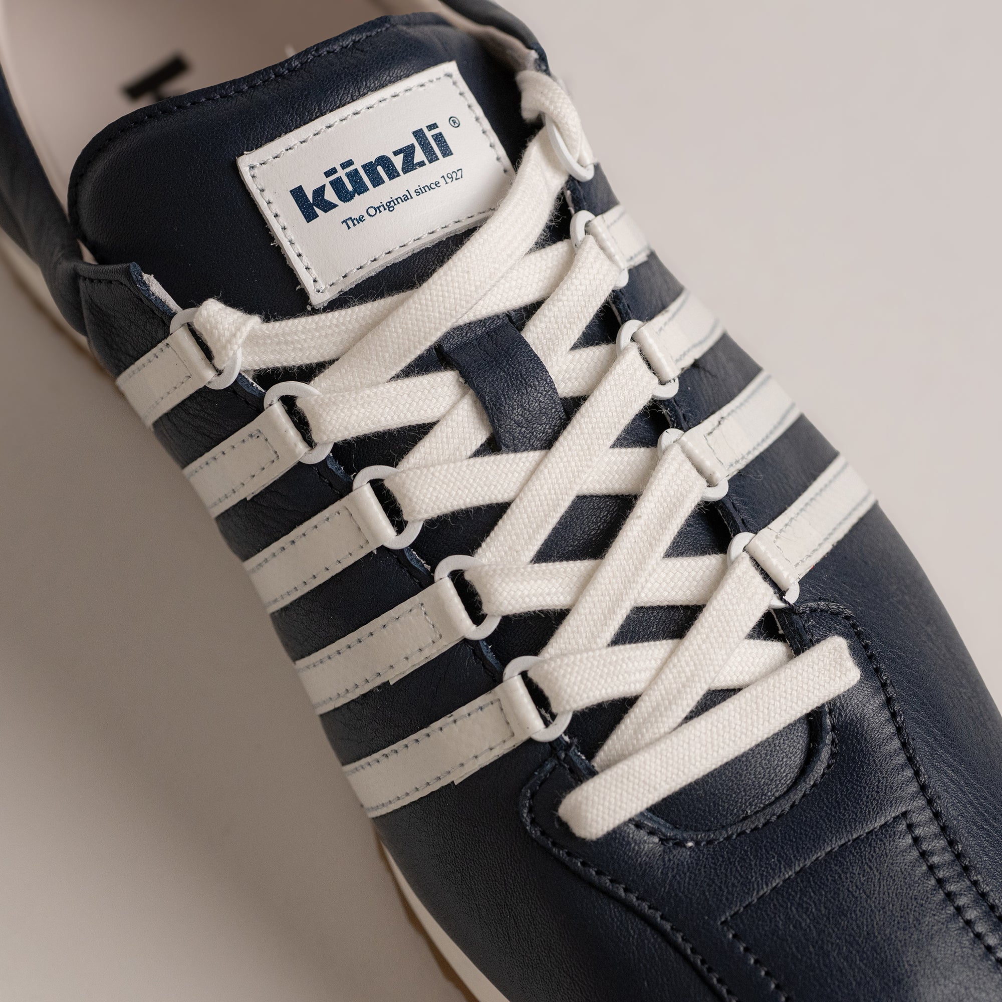 Dunkelblauer Lederschuh von Kuenzli Schuhe mit weißen Streifen und Schnürsenkeln.