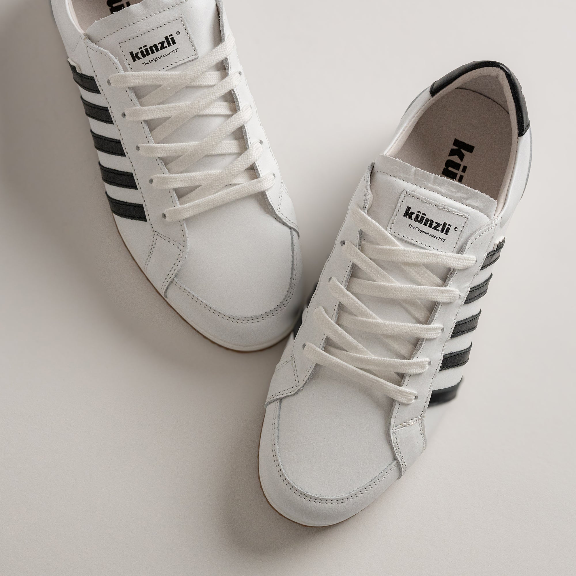 Weiße Kuenzli Schuhe mit schwarzen Streifen auf hellem Hintergrund, sportlich und stilvoll.