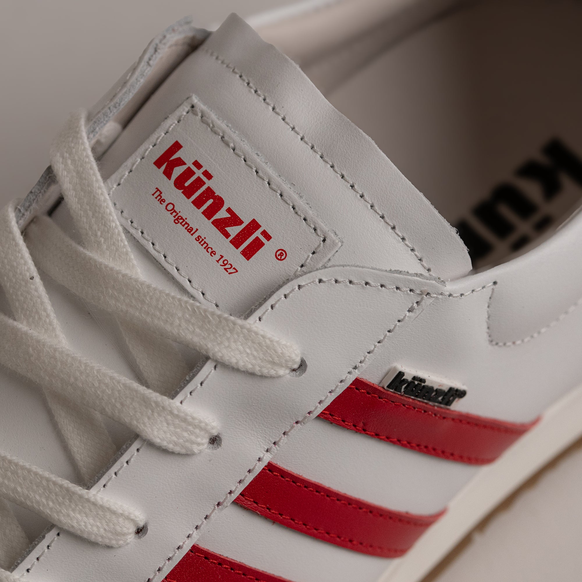 Weißer Kuenzli Schuh mit roten Streifen und Logo, aus Leder gefertigt.