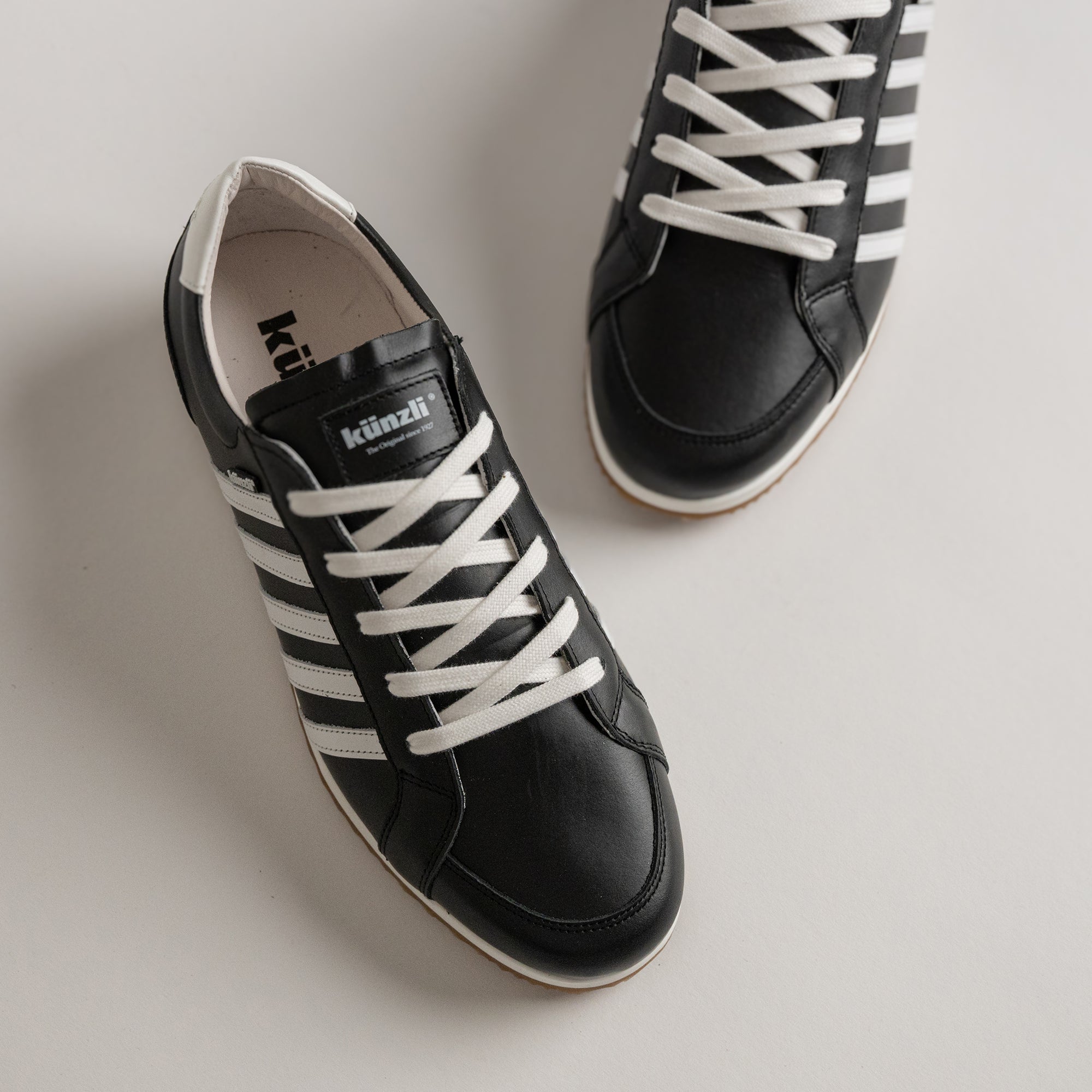 Schwarze Kuenzli Schuhe mit weißen Streifen und Schnürsenkeln auf hellem Hintergrund.