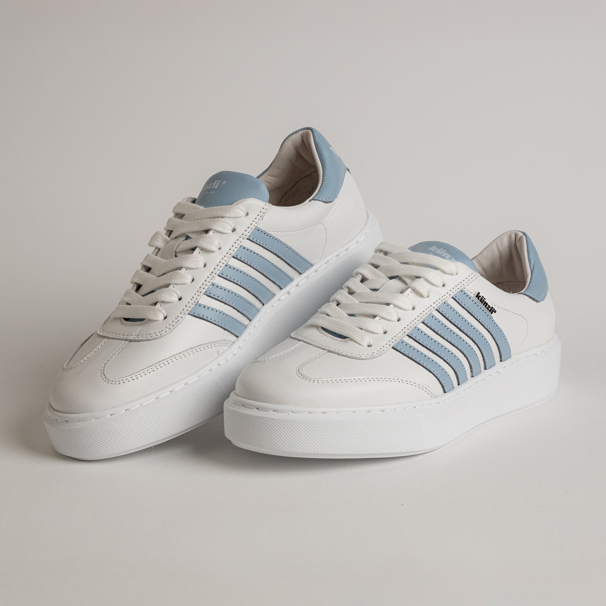 Weiße Kuenzli Schuhe mit blauen Streifen auf hellem Hintergrund, sportlich und modern.