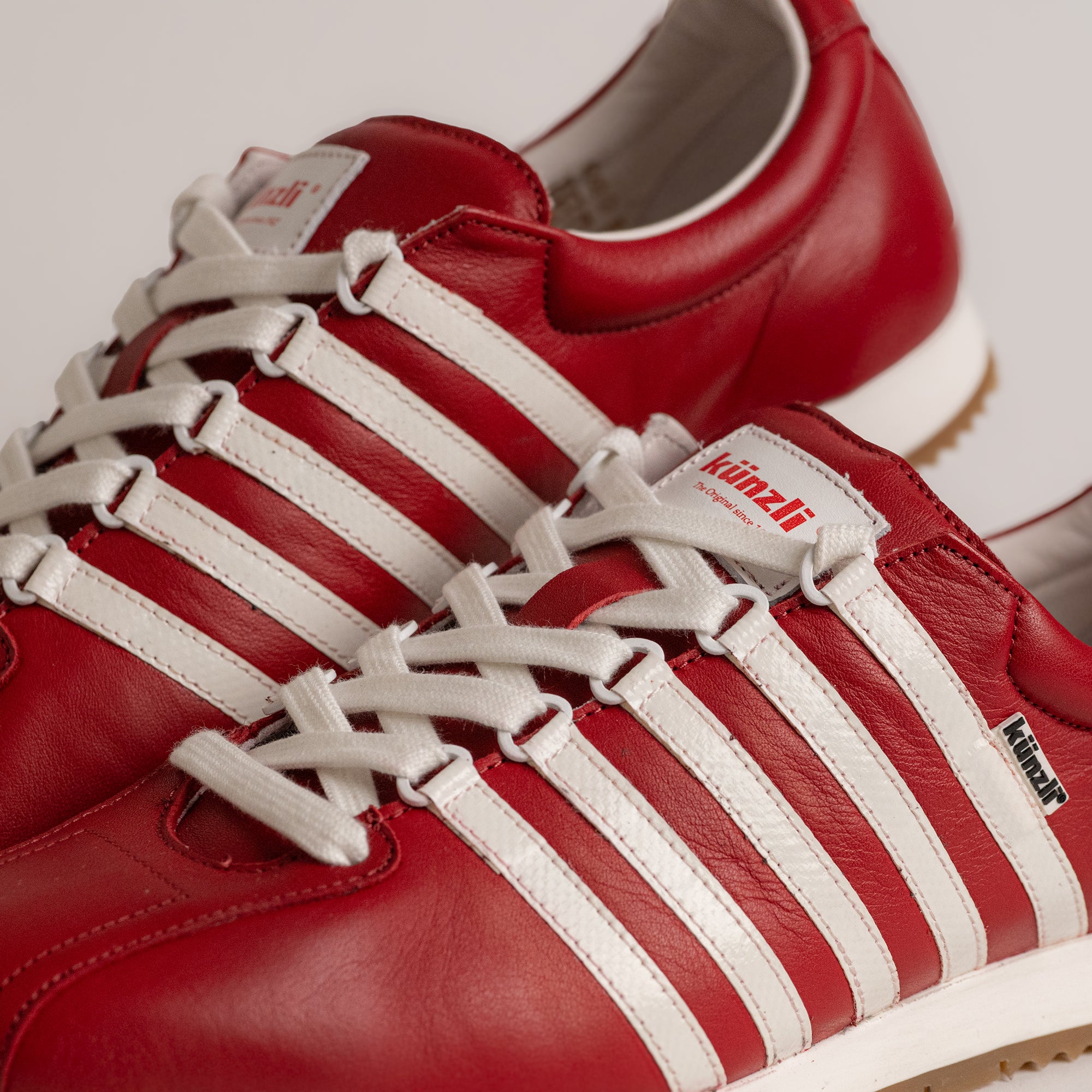 Rote Kuenzli Schuhe aus Leder mit weißen Streifen und Schnürsenkeln, sportliches Design.